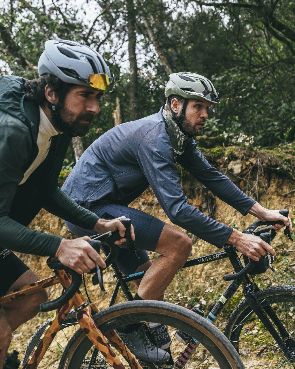 Two cyclists on gravel bikes in forest setting wearing cycling apparel and helmets