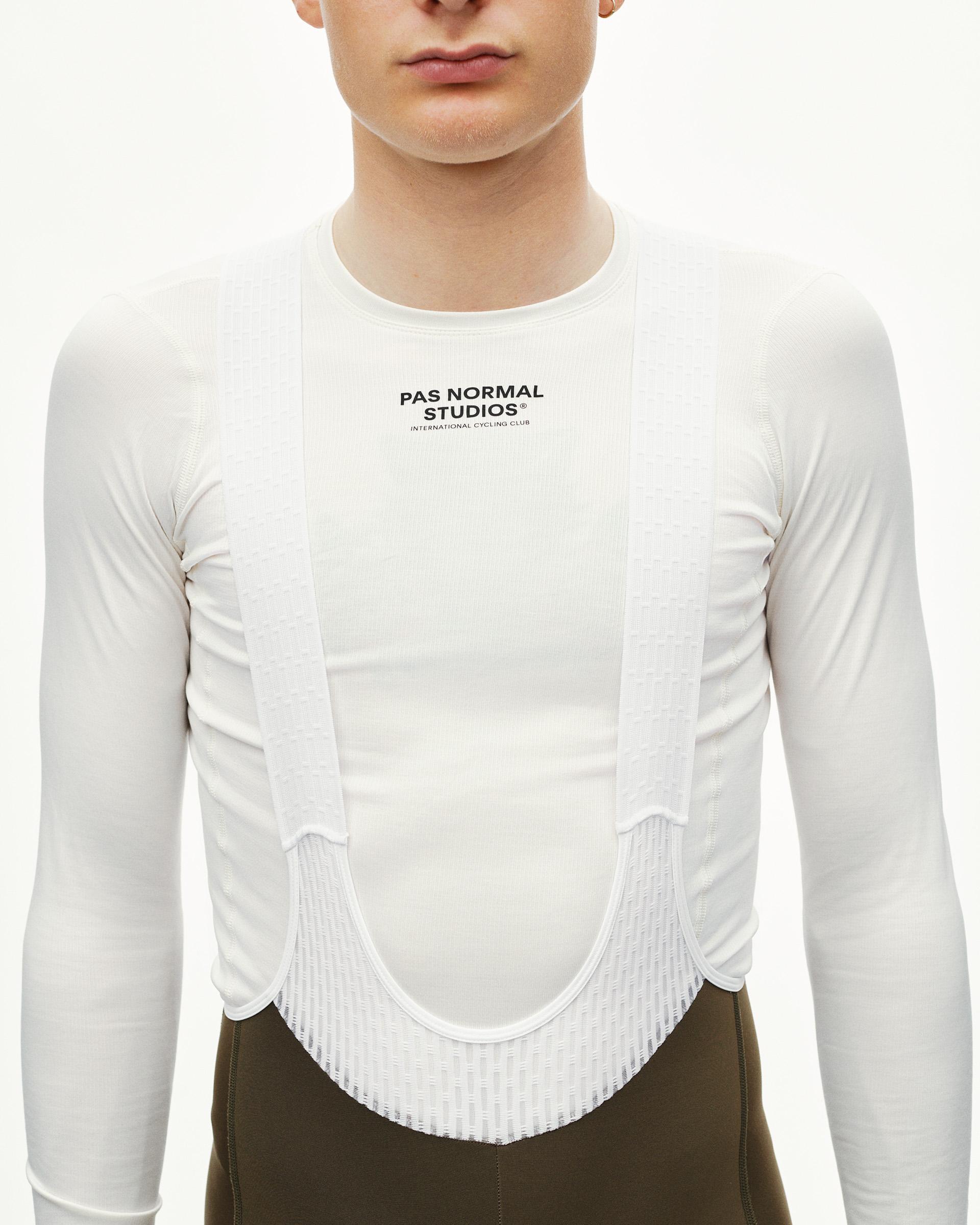 Dark Earth olive thermal long bib tights with a white long-sleeve base layer, shown on a model from the front