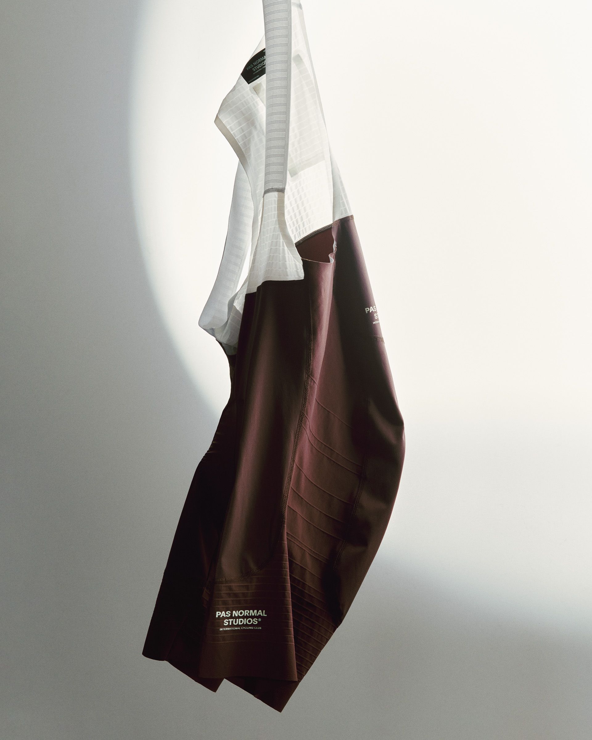 Mechanism Pro cycling garments hanging in studio, white base layer with burgundy shorts featuring leg panels