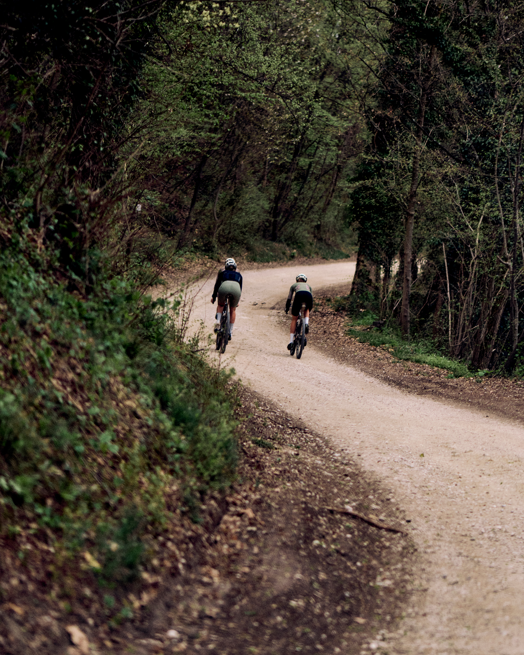 Two cyclists riding on gravel path through wooded tunnel
