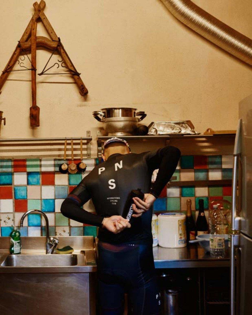 Model wearing black long sleeve jersey with chest branding in kitchen setting