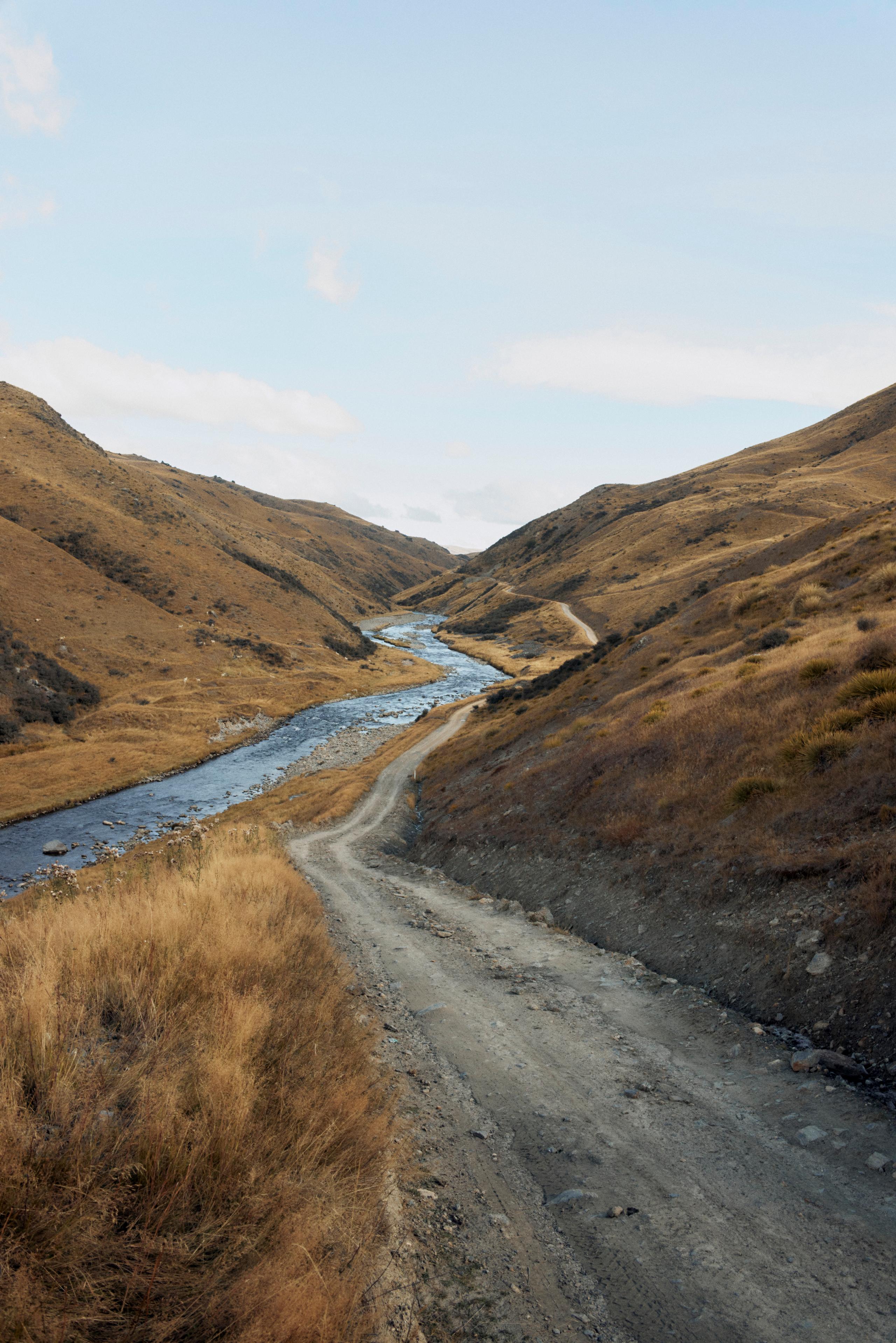 Winding gravel road through golden hills following river valley under cloudy sky