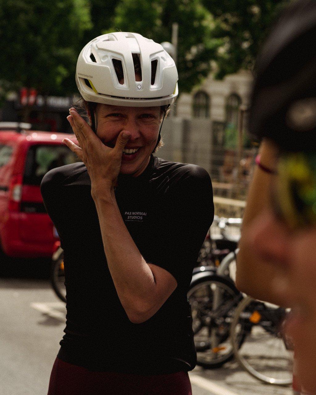 Model wearing black cycling jersey with logo and white helmet on city street