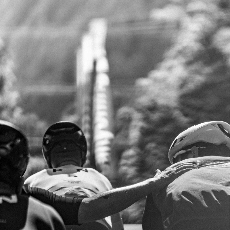 Three cyclists with helmets viewed from behind in black and white, overlooking urban landscape