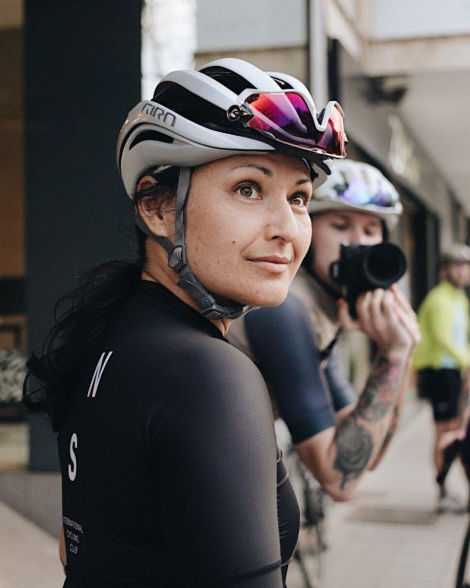 Female cyclist in white aerodynamic helmet and black jersey looking over shoulder