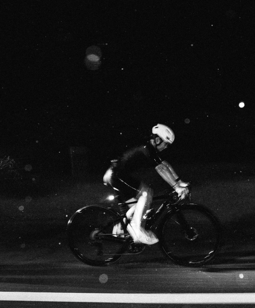Cyclist in aerodynamic position riding at night in black and white photograph