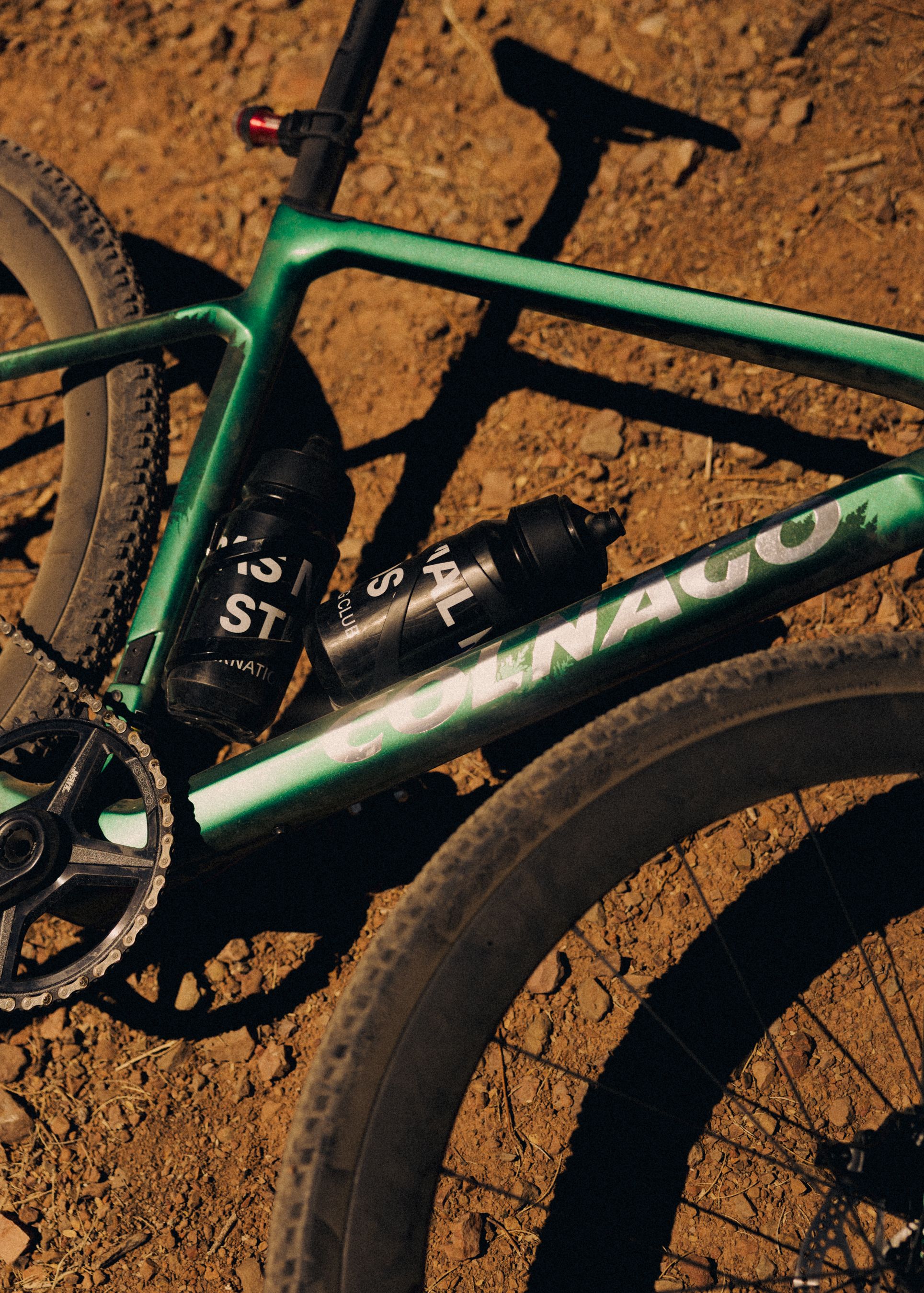 Green gravel bike frame with water bottles on dirt terrain