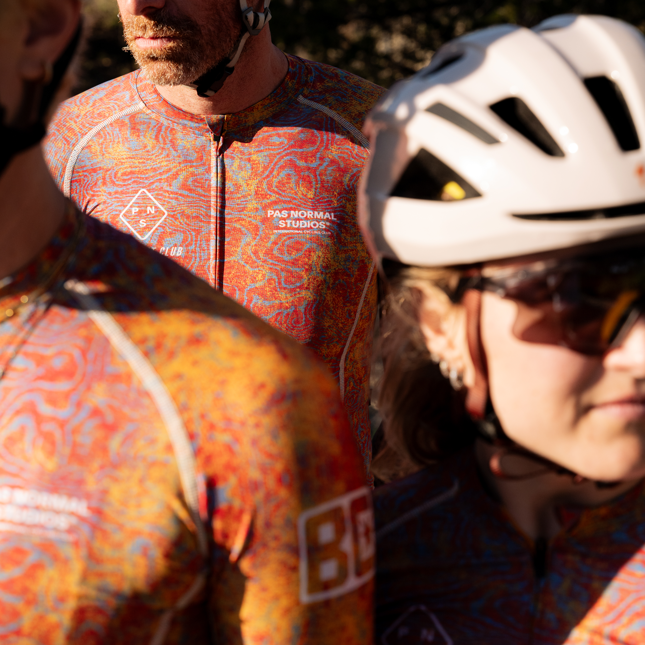 Model wearing orange patterned cycling jersey with colorful abstract print and logo branding