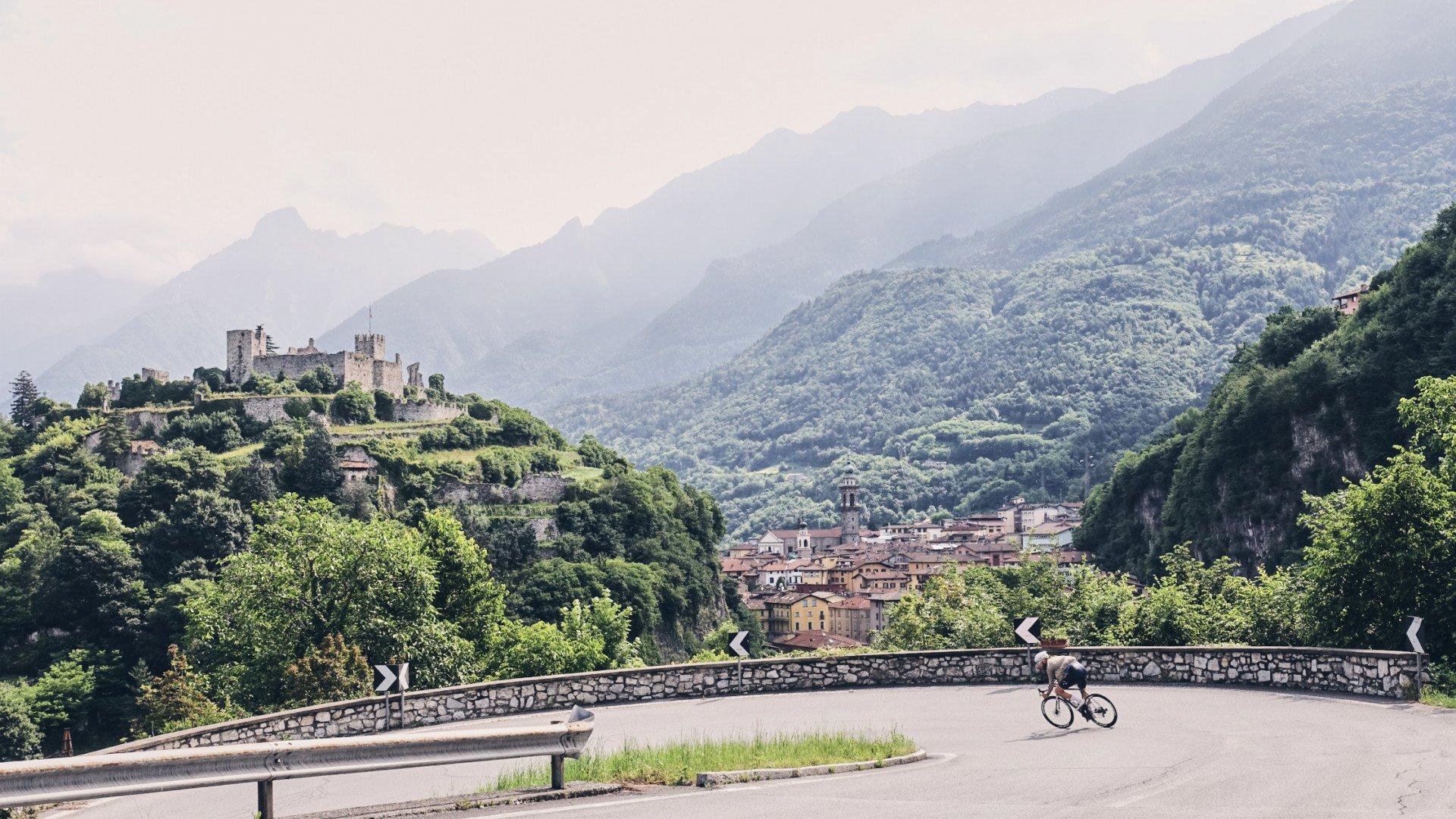 Cyclist on mountain road with Italian hillside town and castle in background