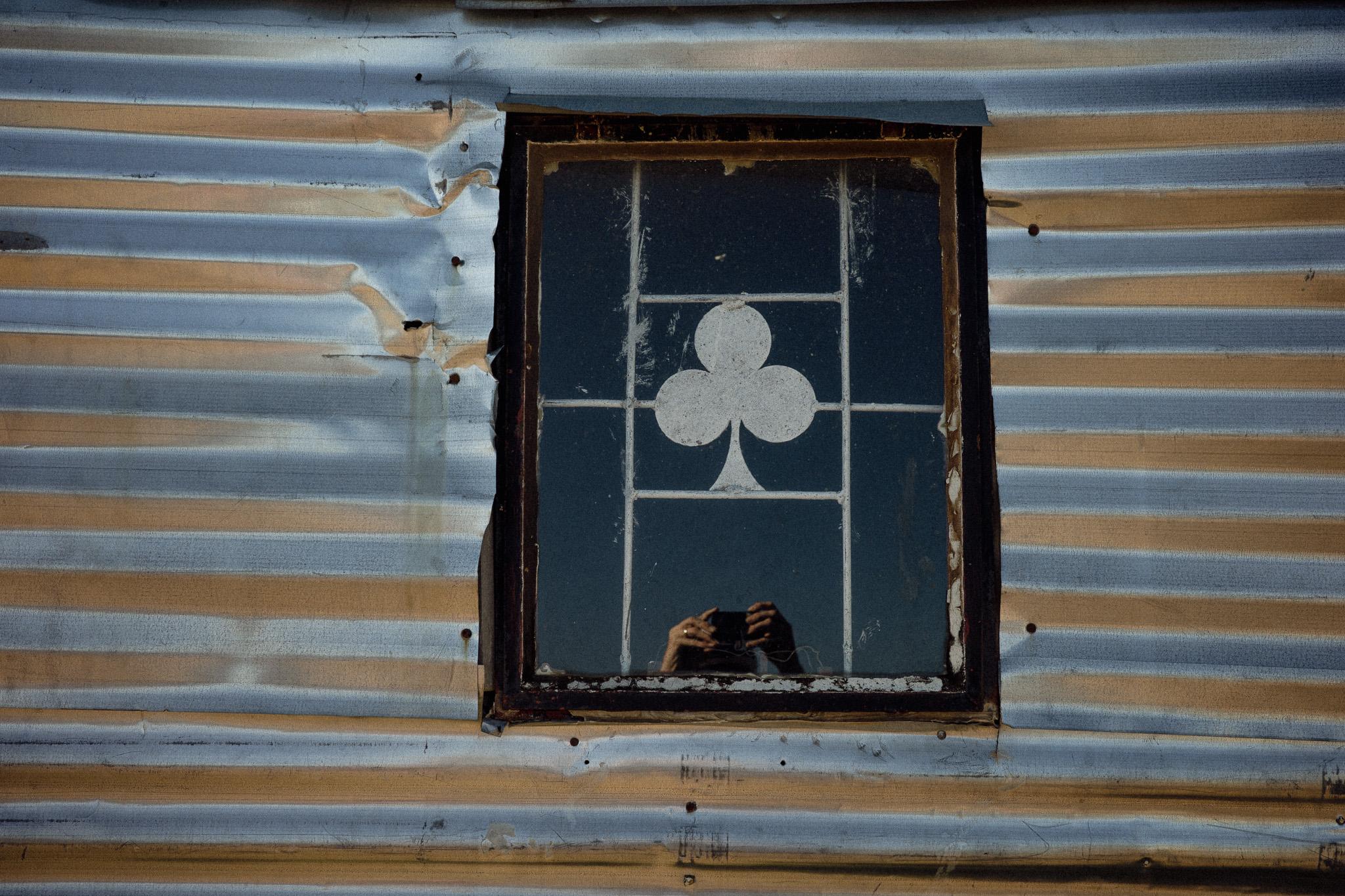 Weathered window with club symbol in corrugated metal building, Lesotho