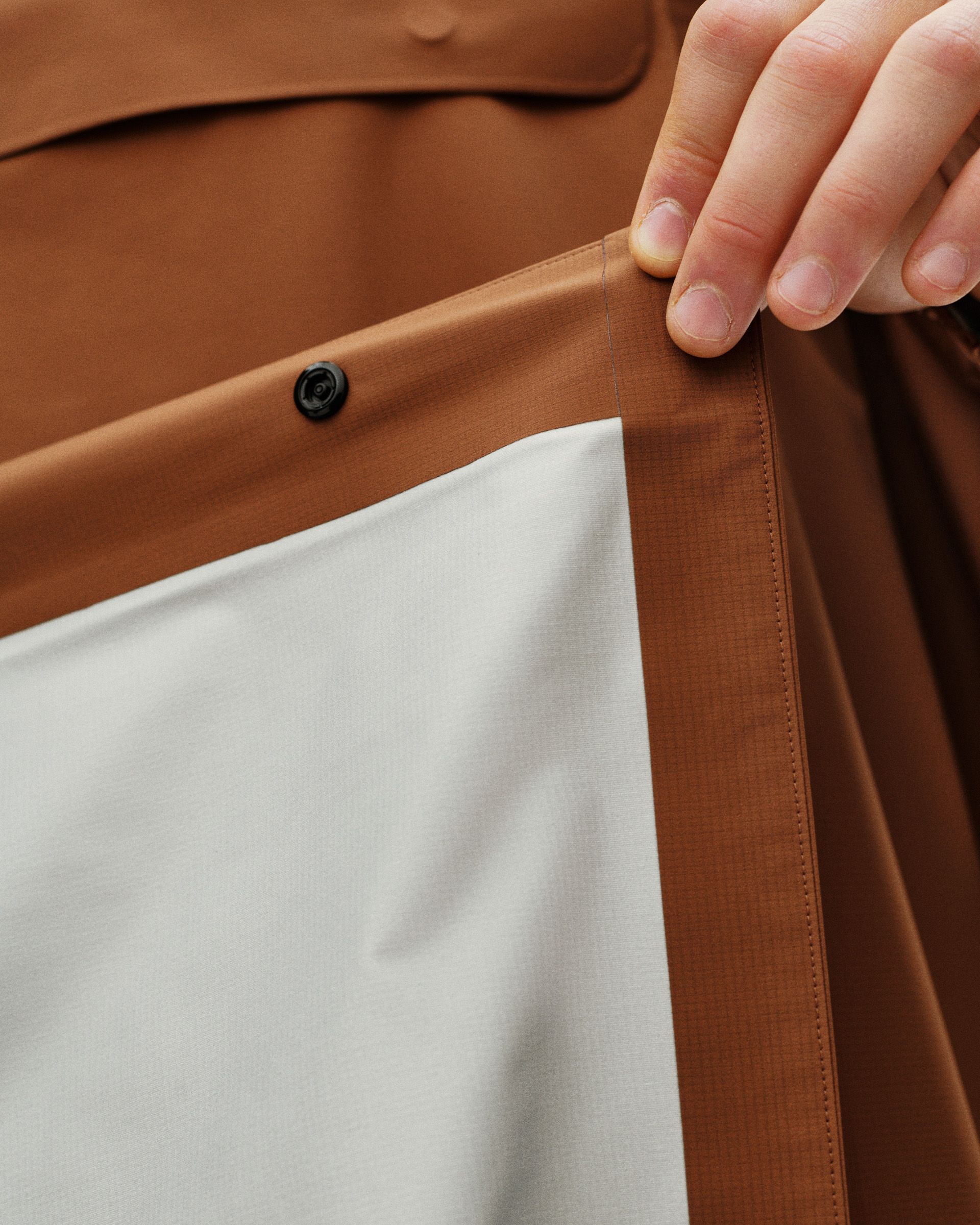 Hand touching taped seam on waterproof jacket with hydrophobic membrane for breathability and weather protection