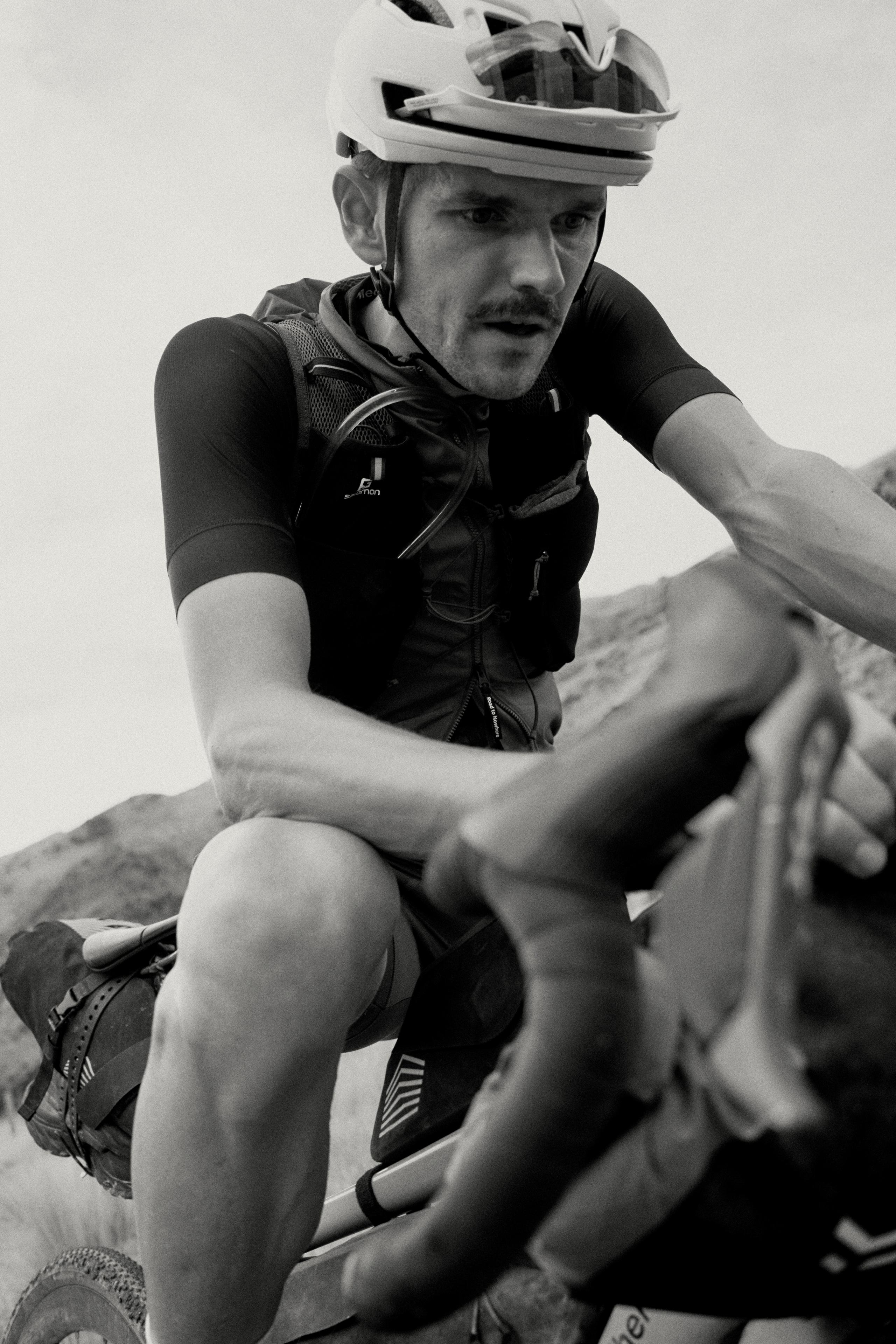 Model wearing black cycling jersey with hydration pack, sitting on rocky terrain