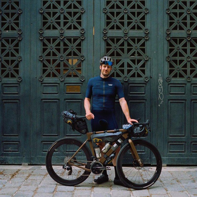 Model wearing blue cycling jersey and shorts with bike against ornate green doors