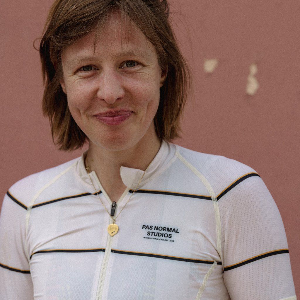 Model wearing white cycling jersey with horizontal black stripes and chest branding against pink background