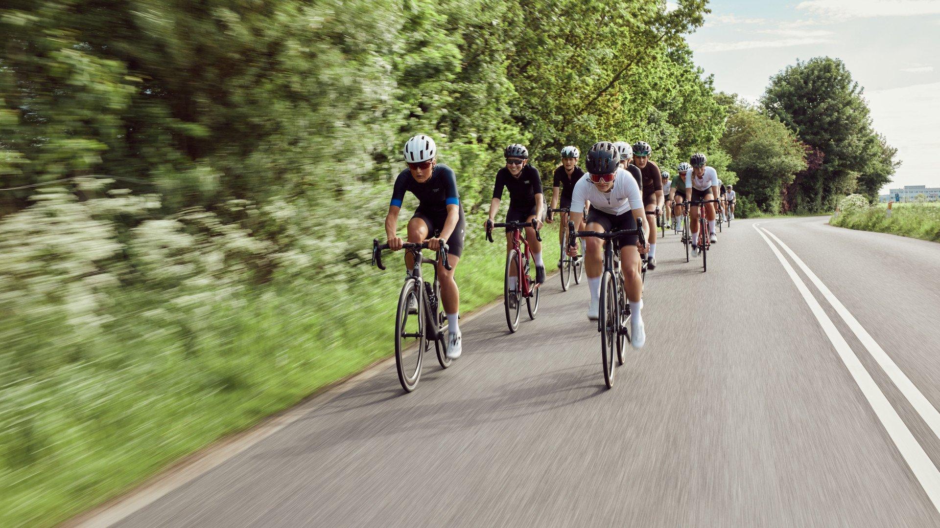 Group of cyclists in aerodynamic position riding on country road through green landscape