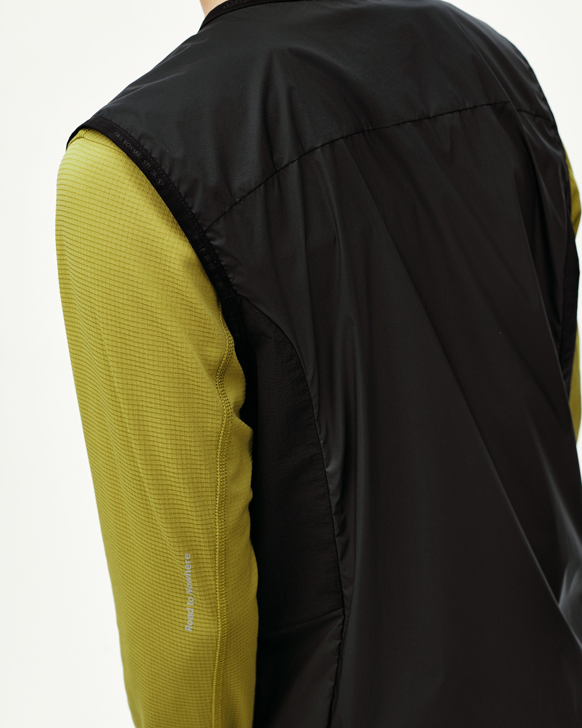 Black Balance Windproof Vest on model, rear detail view with olive ribbed sleeve contrast
