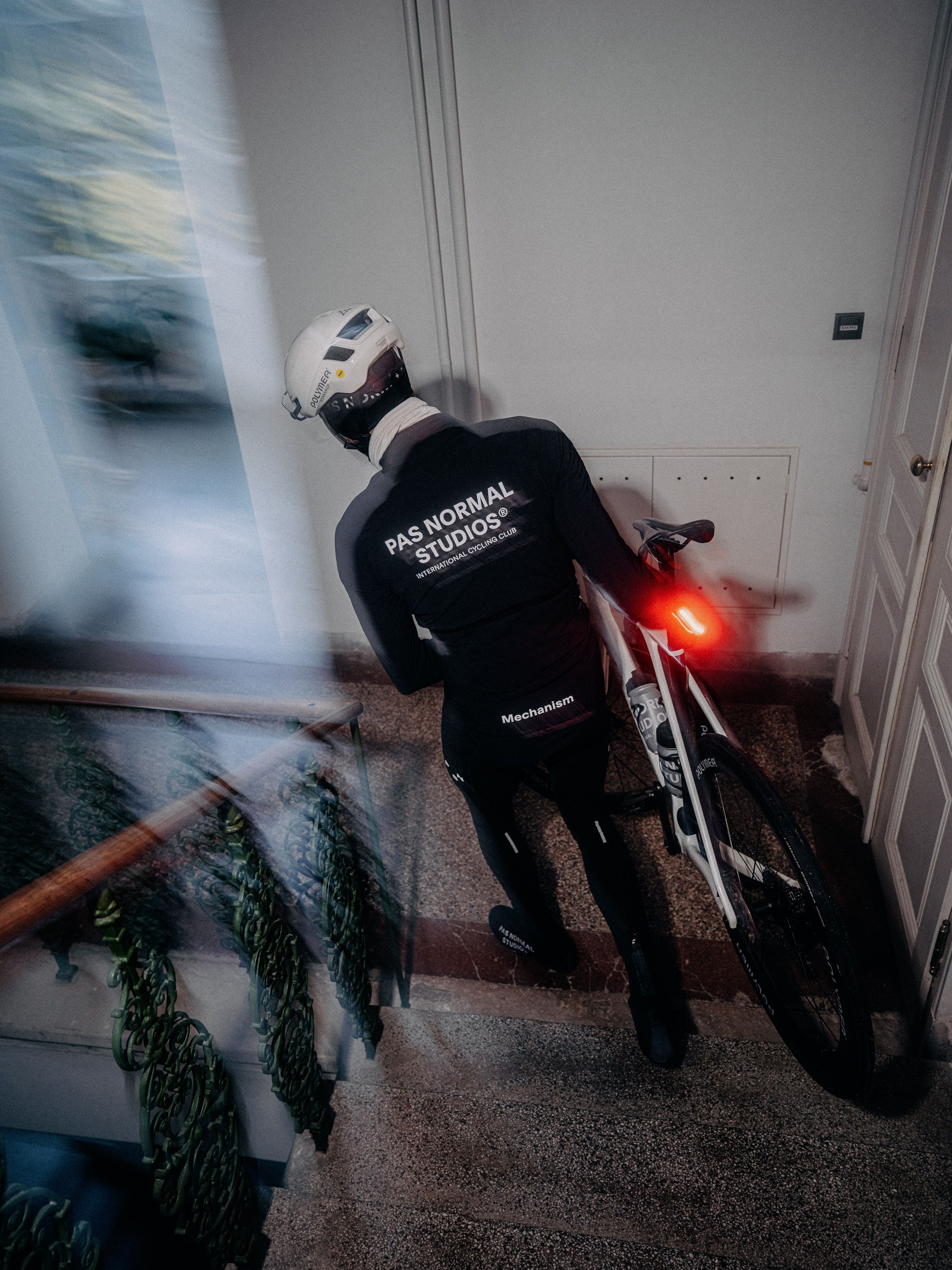 Model wearing black Mechanism jersey with back branding, helmet, riding bike indoors with motion blur