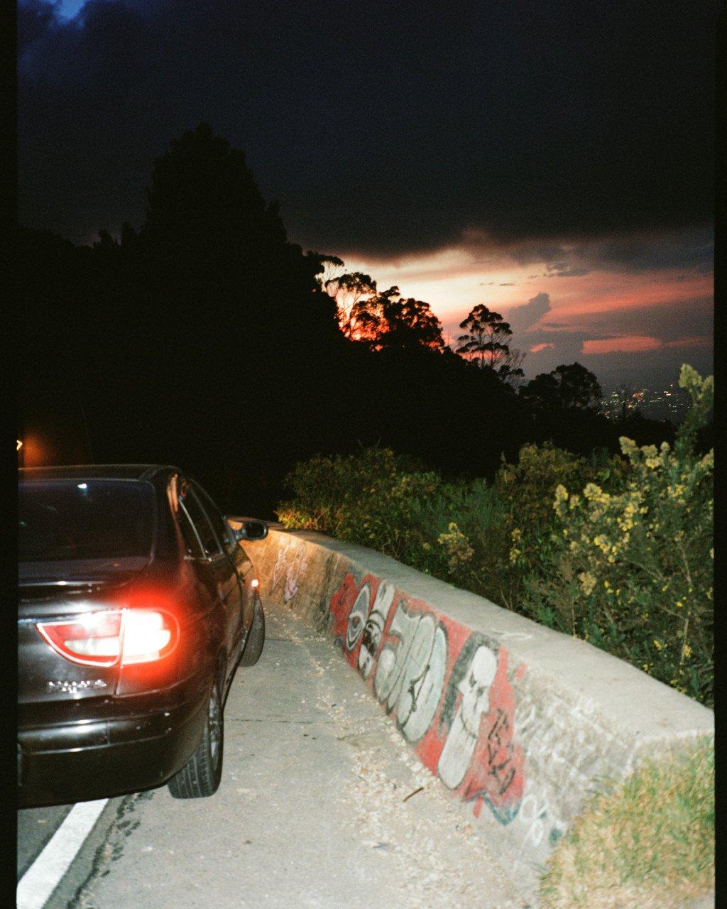 Car parked beside concrete barrier with graffiti at dusk in Bogotá
