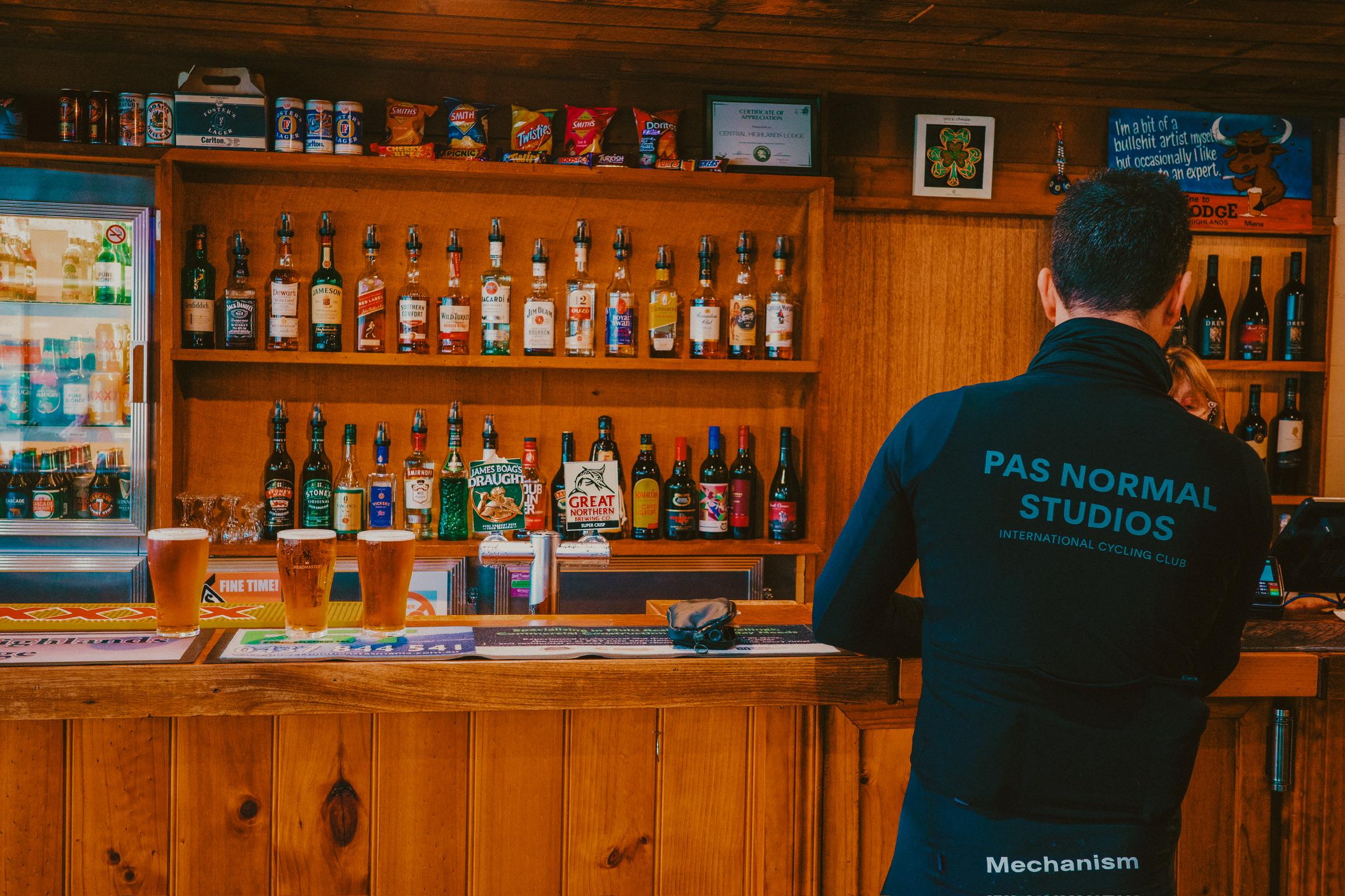 Model wearing black Mechanism jersey with back branding at wooden bar counter