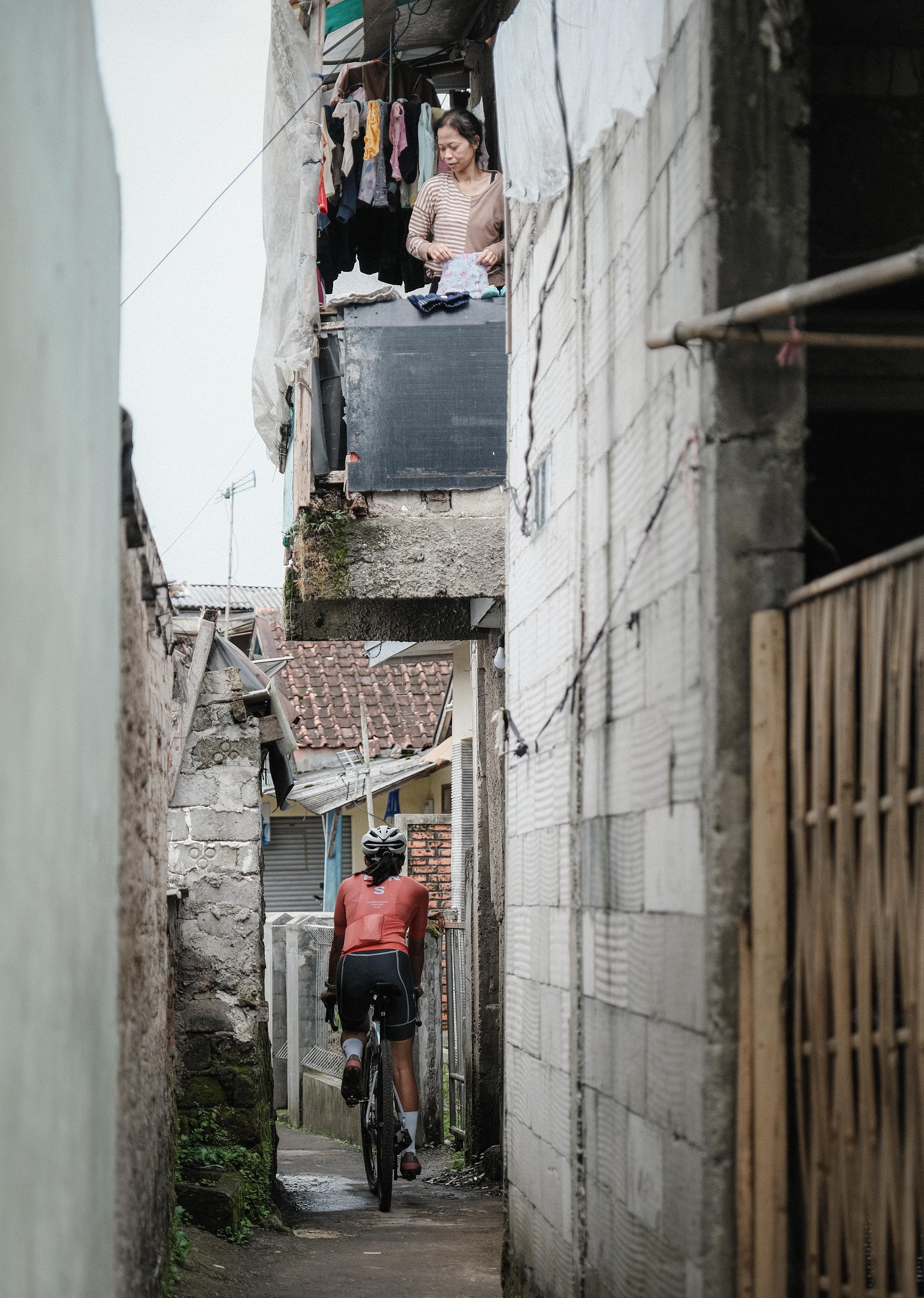 Cyclist in coral jersey and black shorts riding through narrow alley between white stone buildings