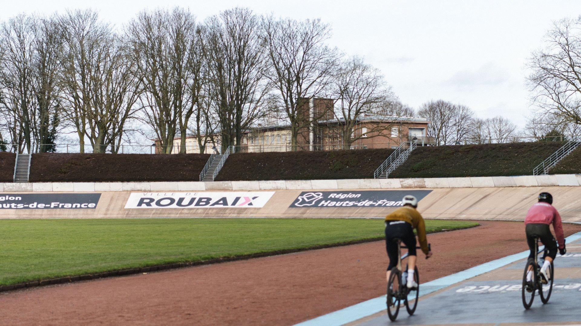 Two cyclists racing on Roubaix velodrome track in yellow and pink jerseys