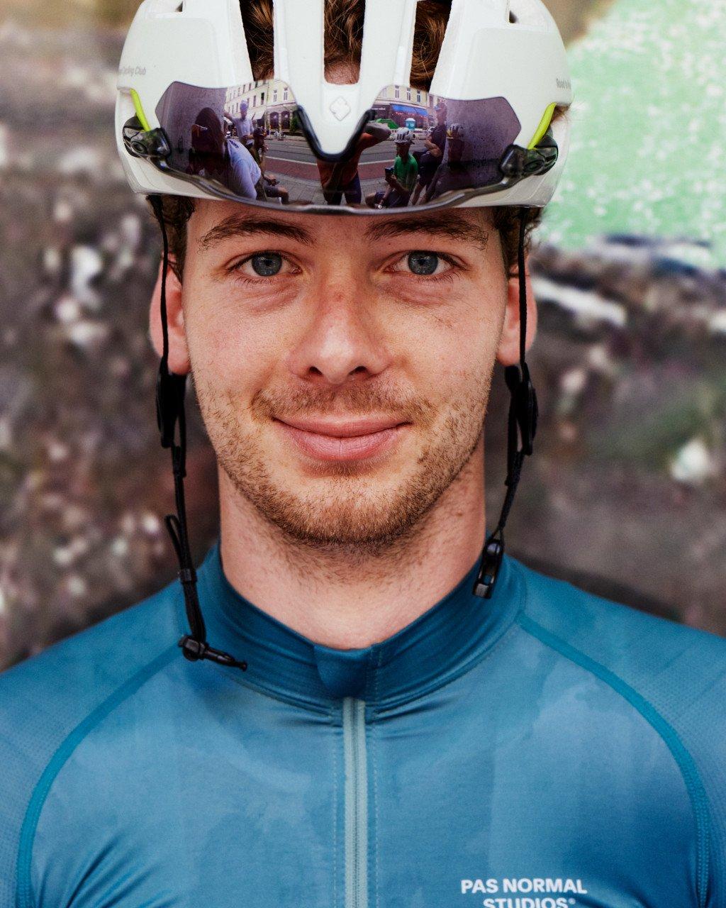Model wearing blue cycling jersey and white helmet with mirrored visor reflecting street scene