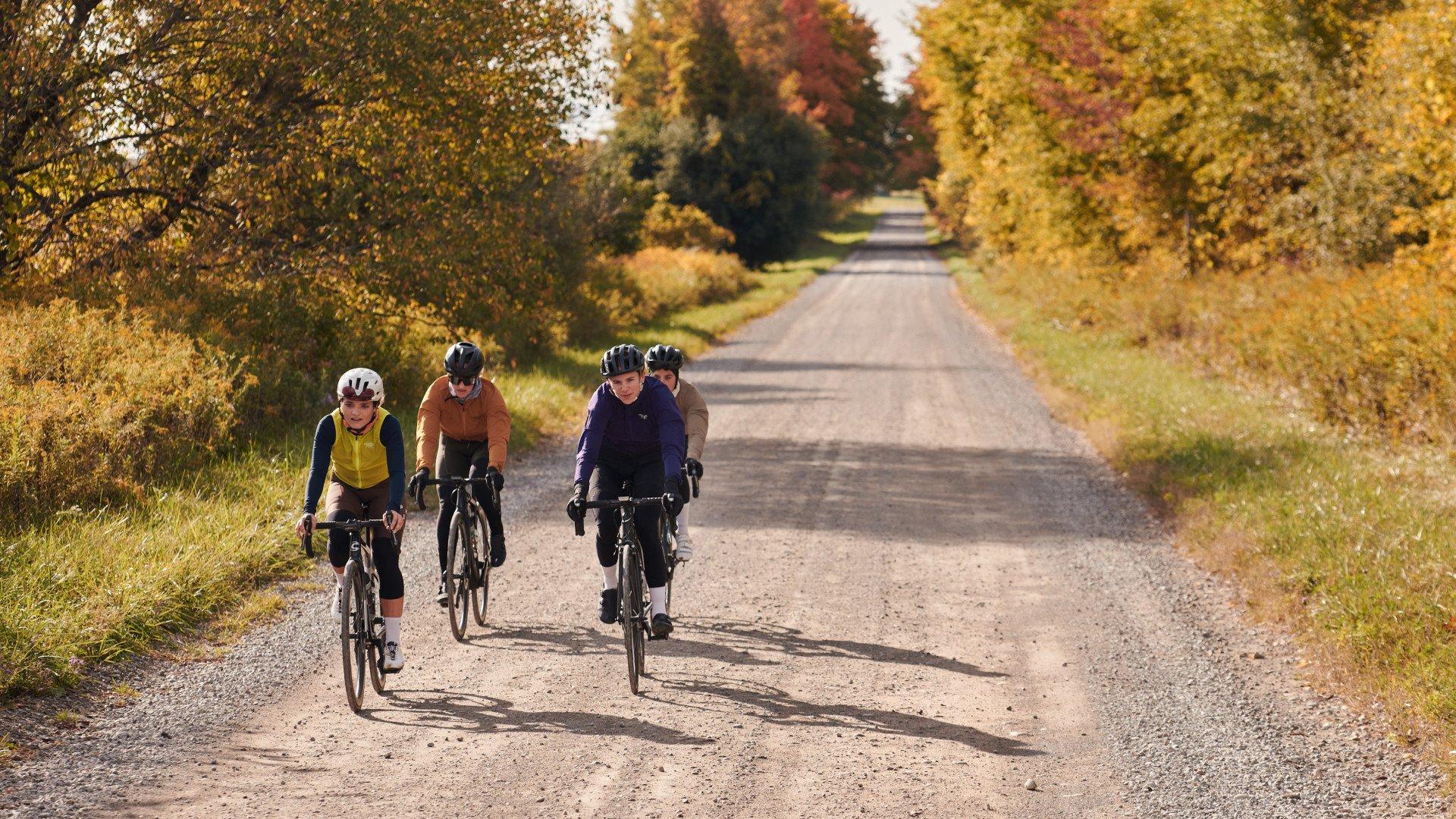 Four cyclists in aerodynamic position riding gravel road through autumn landscape with golden foliage