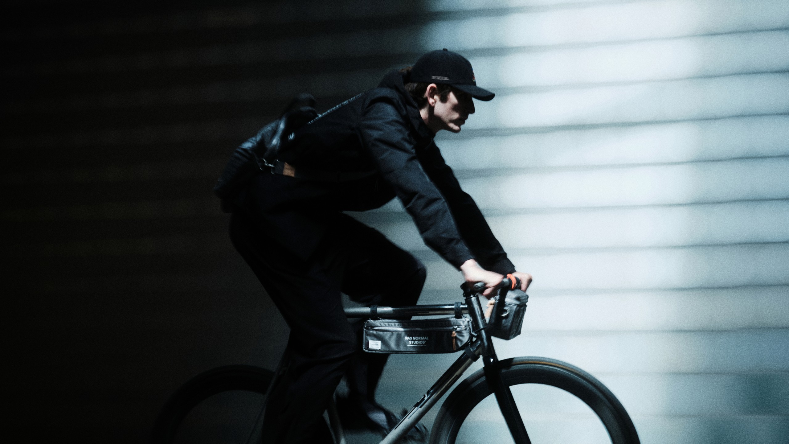 Model wearing black cycling outfit with cap, riding bike with front bag in motion blur shot