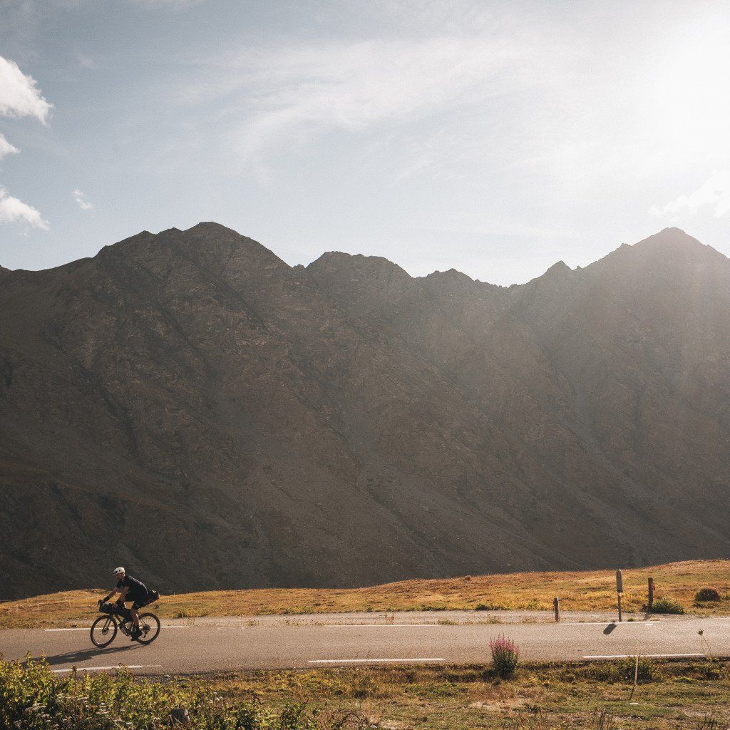 Cyclist riding through mountain landscape with dramatic peaks and golden grassland