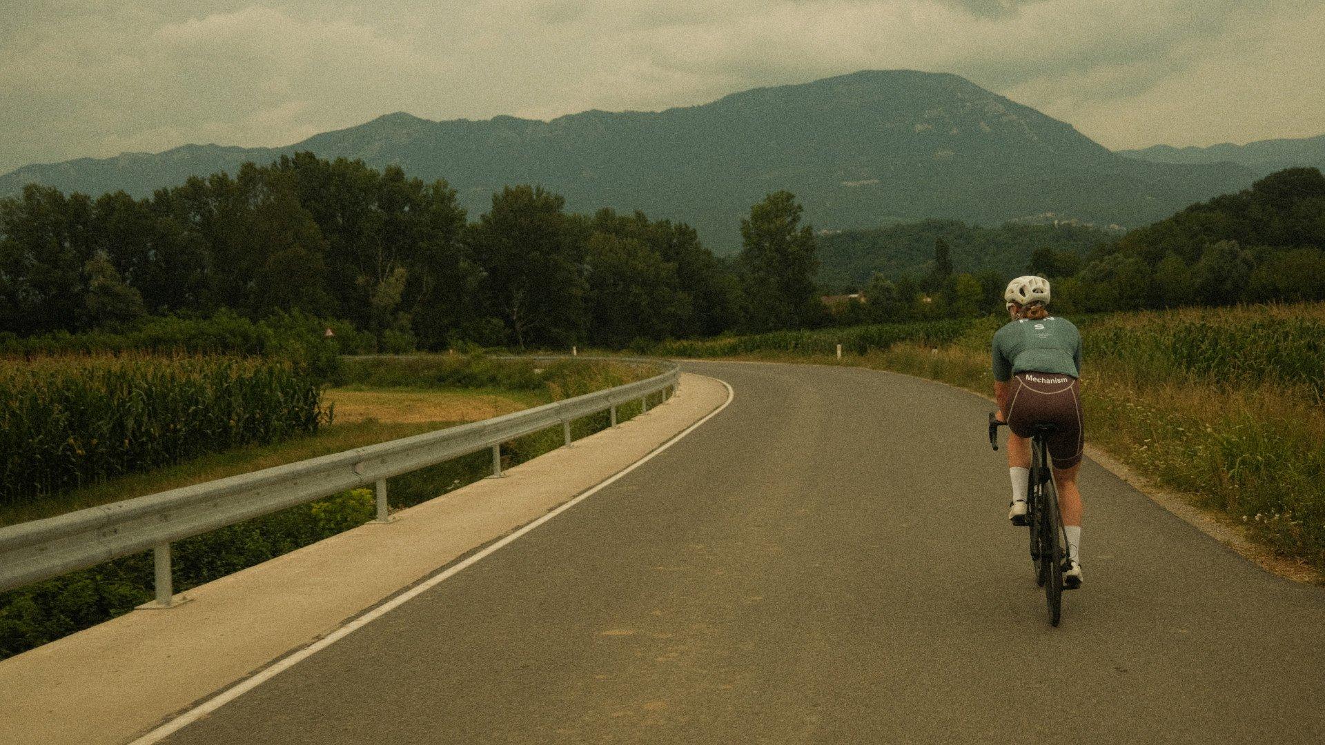 Model wearing grey Mechanism jersey cycling on rural road through Slovenian countryside