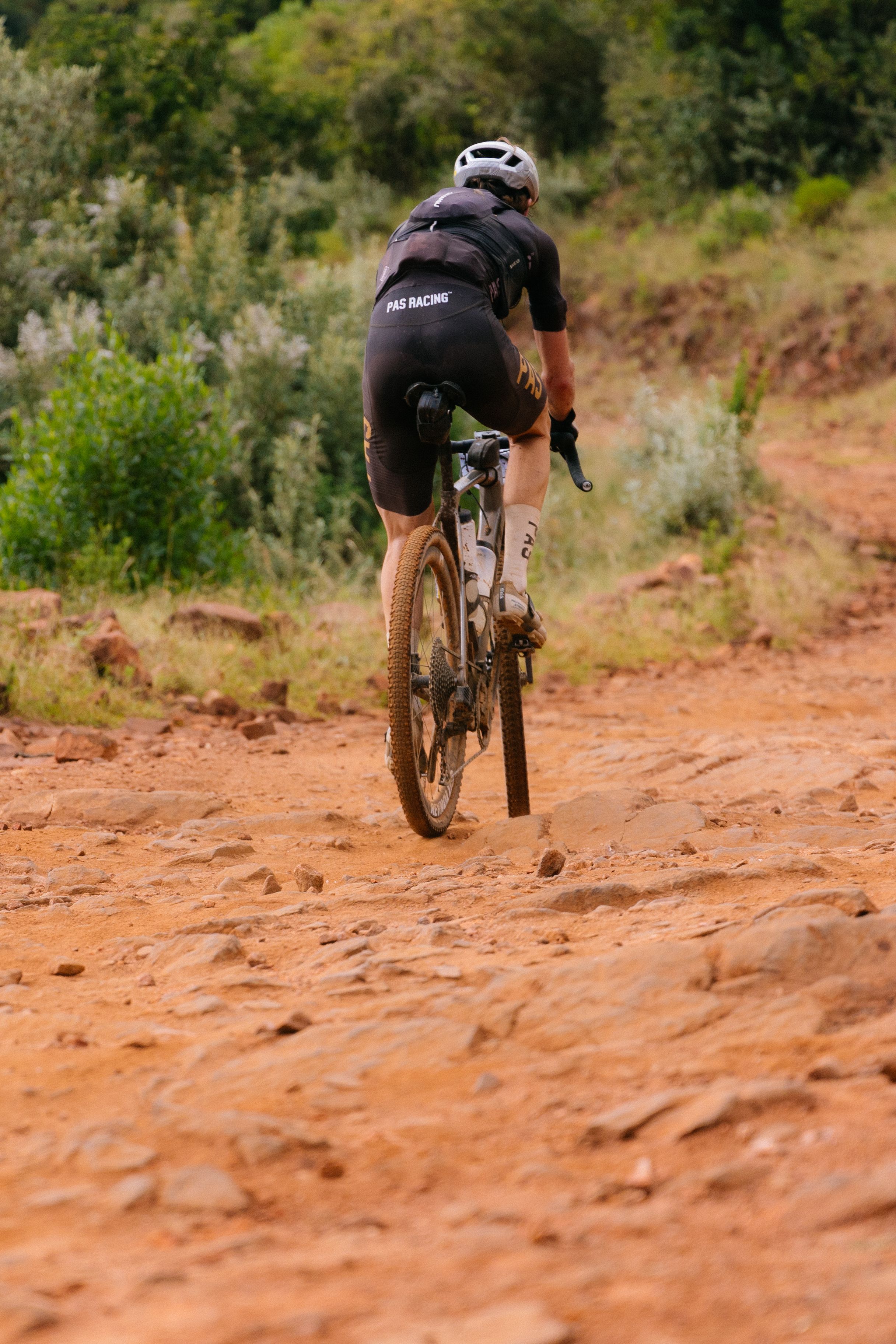 Model wearing black Racing collection jersey and shorts cycling on dirt trail