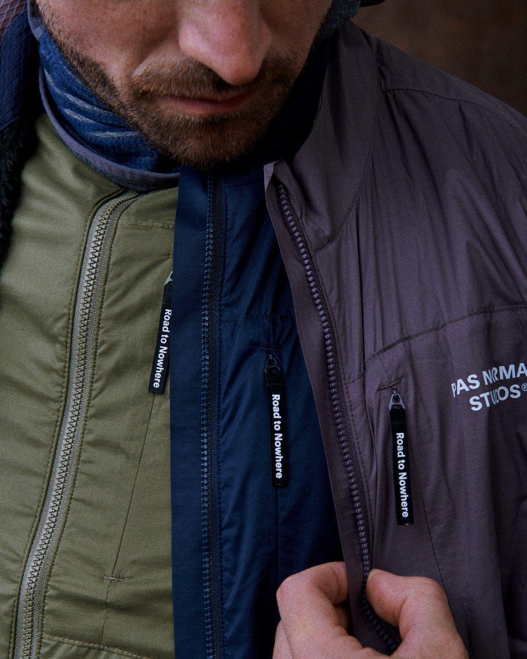 Model wearing layered cycling jackets in olive green, navy blue, and dark grey with full zip closures and chest branding