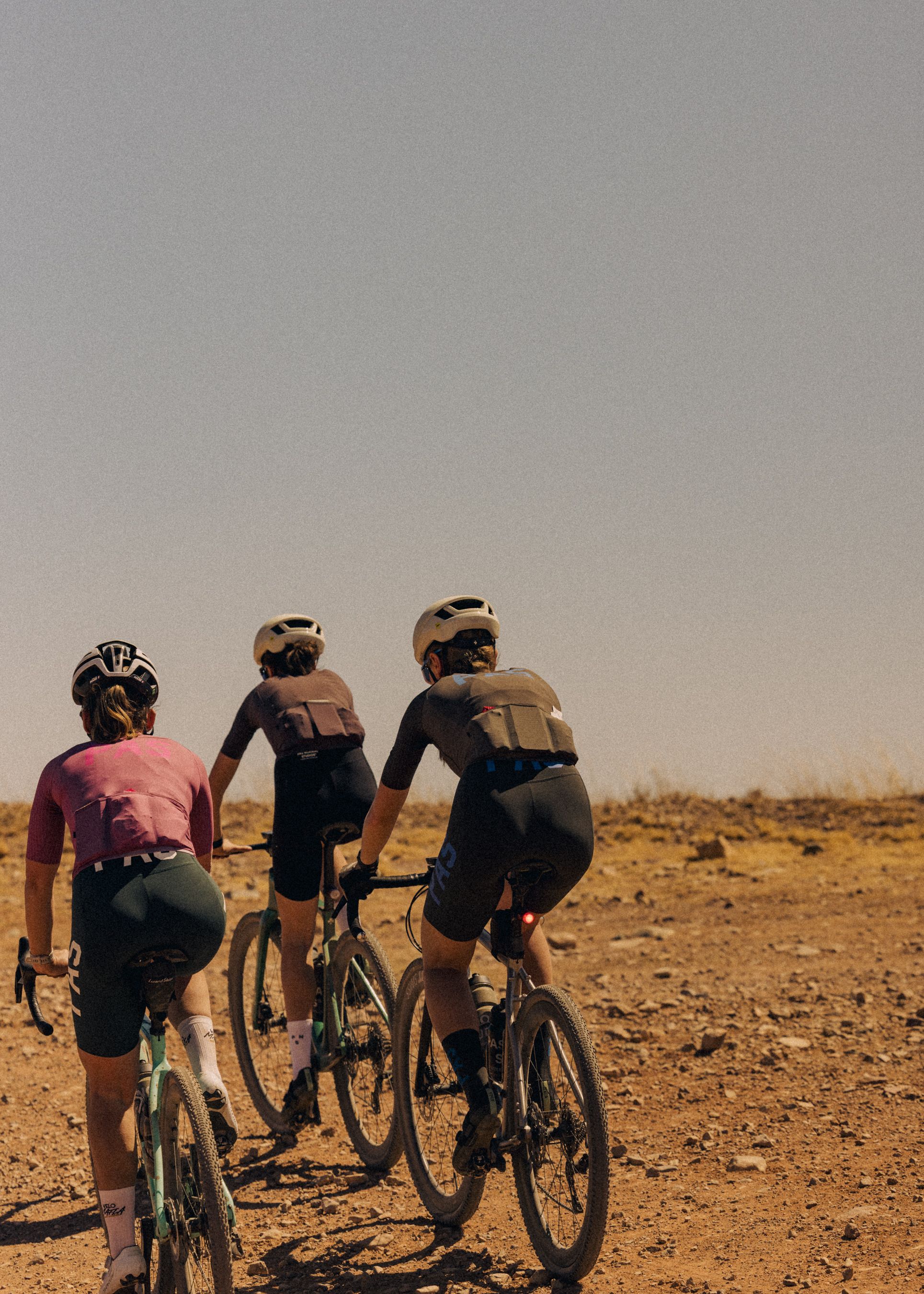 Three cyclists with bikepacking gear riding gravel bikes on desert terrain in warm sunlight