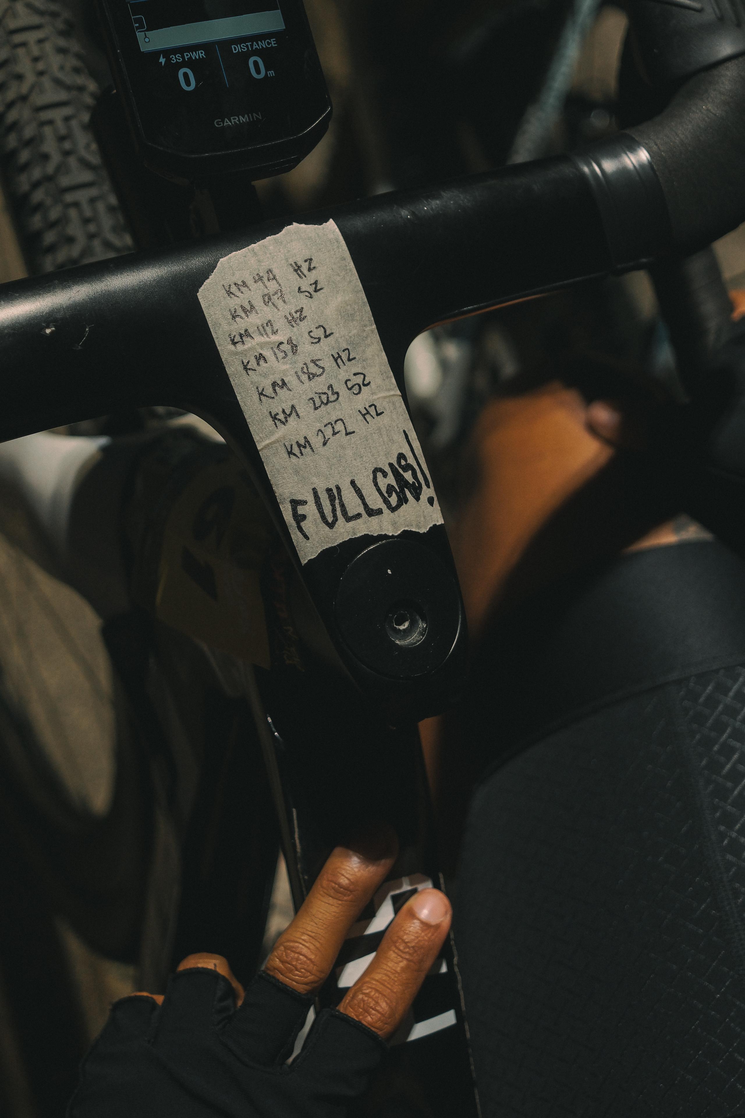 Cycling computer and handlebars with handwritten race note showing kilometer markers