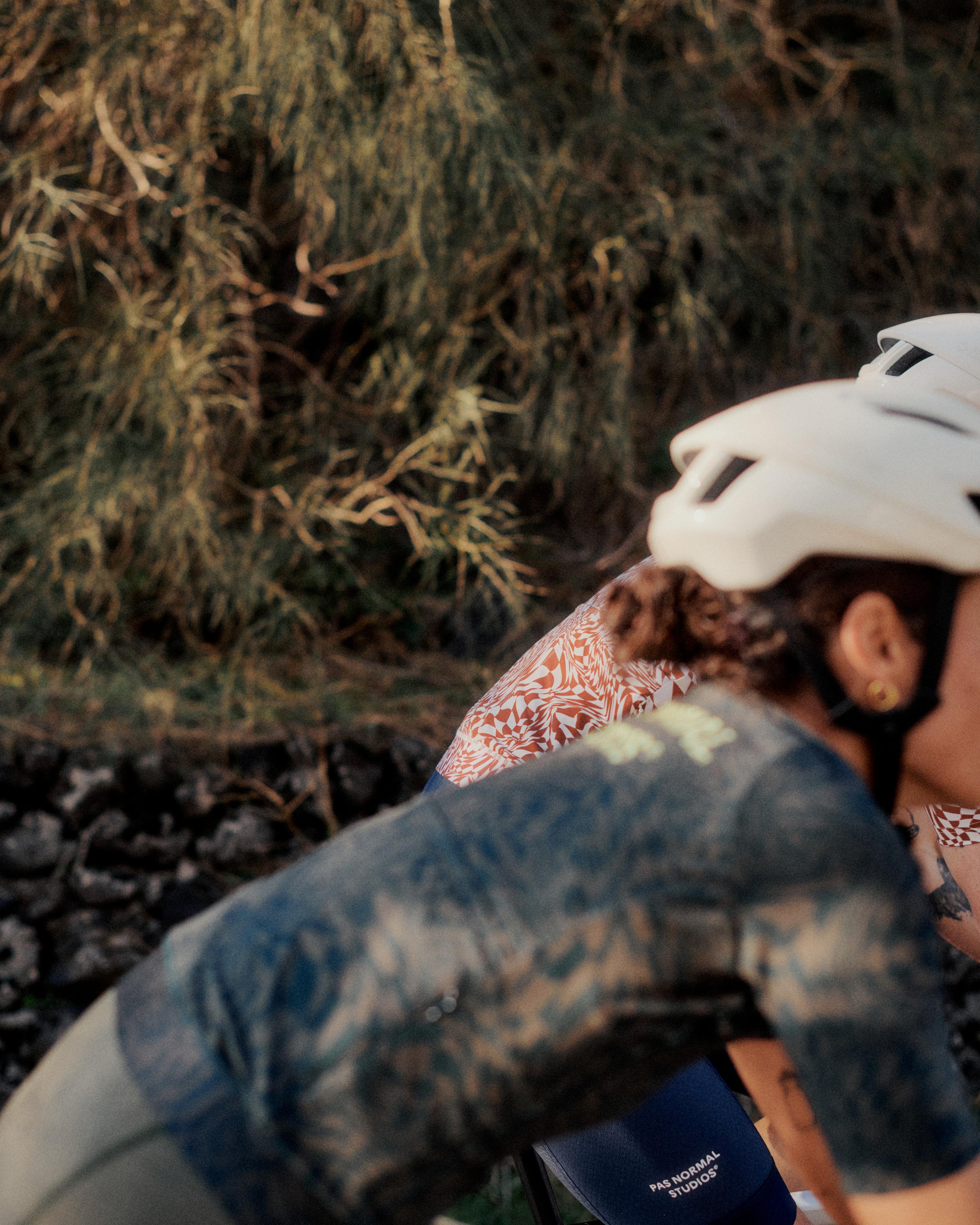 Cyclist wearing white helmet and orange patterned jersey resting against rocky terrain