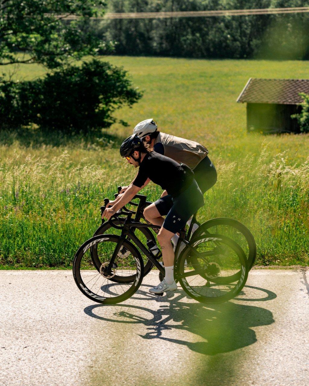 Model wearing black cycling kit on time trial bike in rural countryside setting