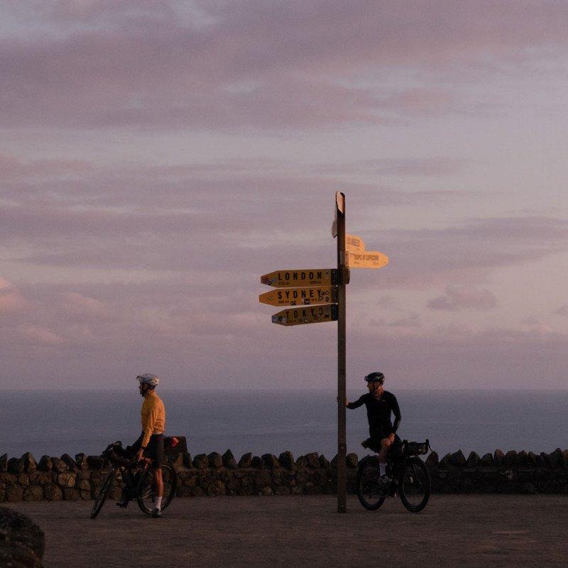 Two cyclists with bikes at directional signpost during golden hour in New Zealand landscape