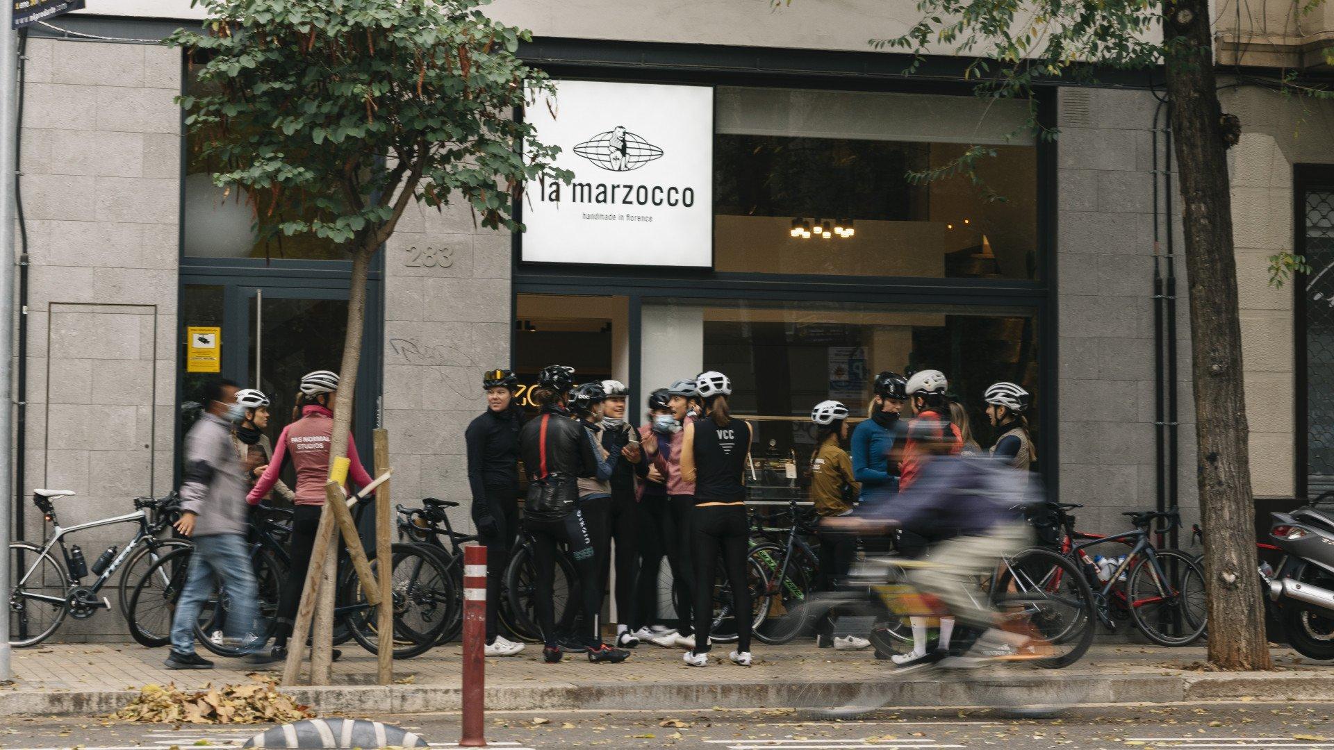 Group of cyclists gathered outside La Marzocco cafe with bikes, wearing colorful cycling apparel and helmets