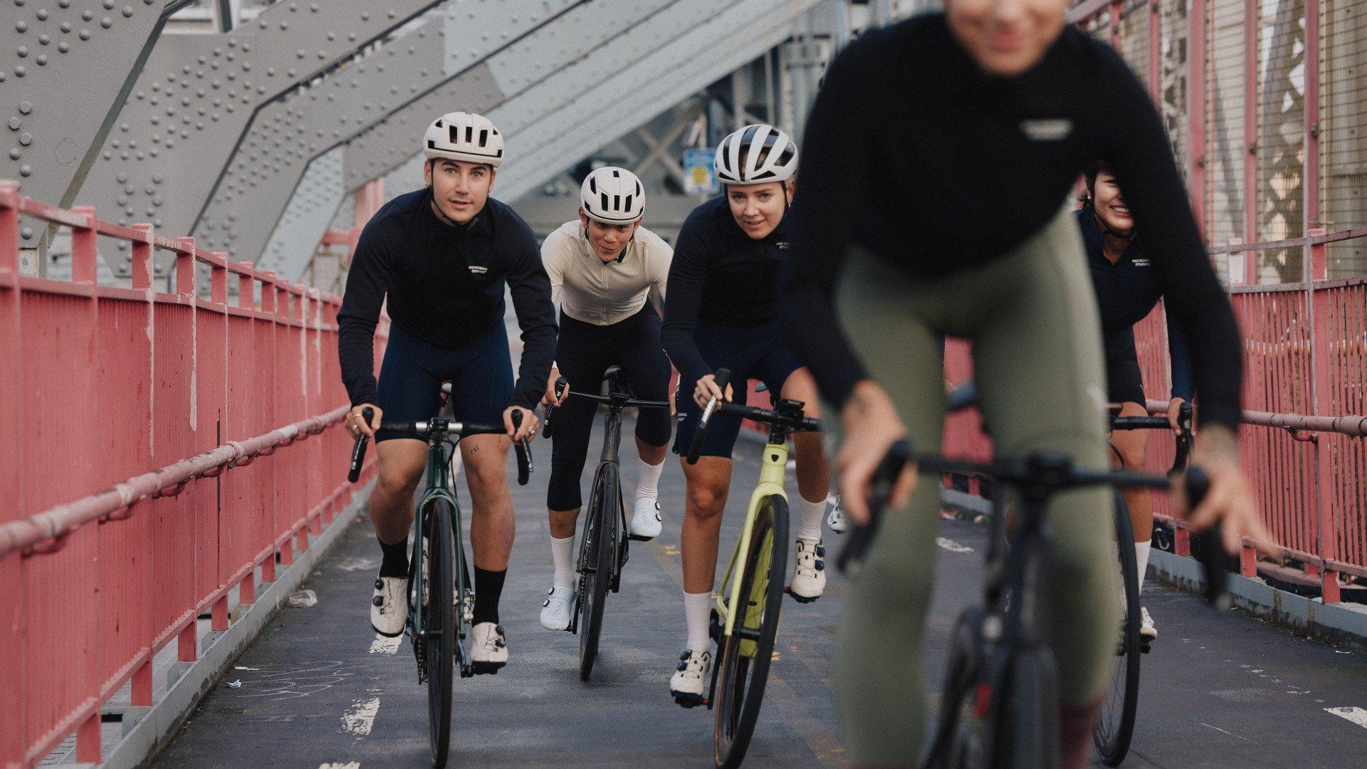 Cyclists wearing mixed colors of cycling apparel riding on red bridge with urban architecture
