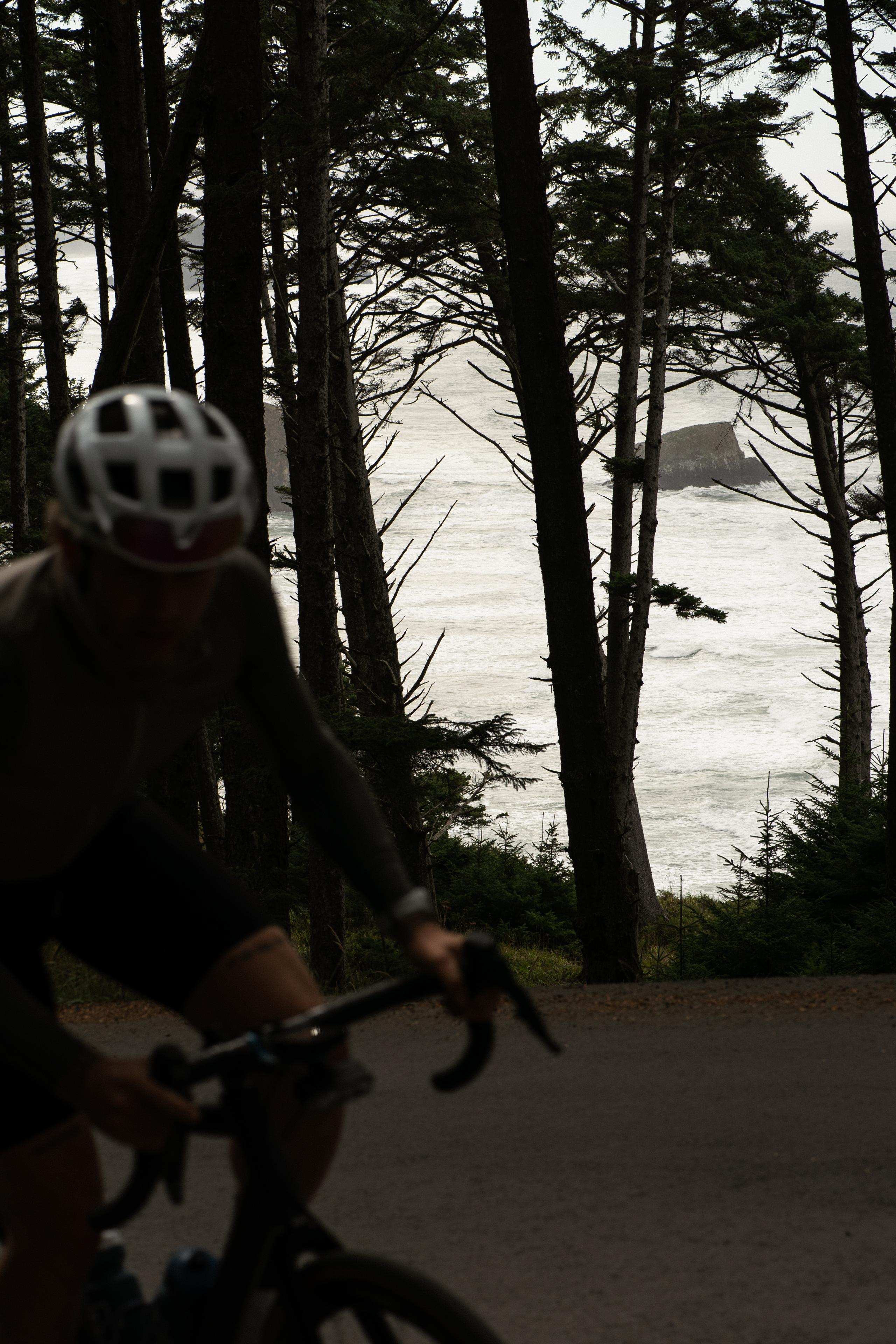 Cyclist with helmet viewing ocean through forest trees on coastal road