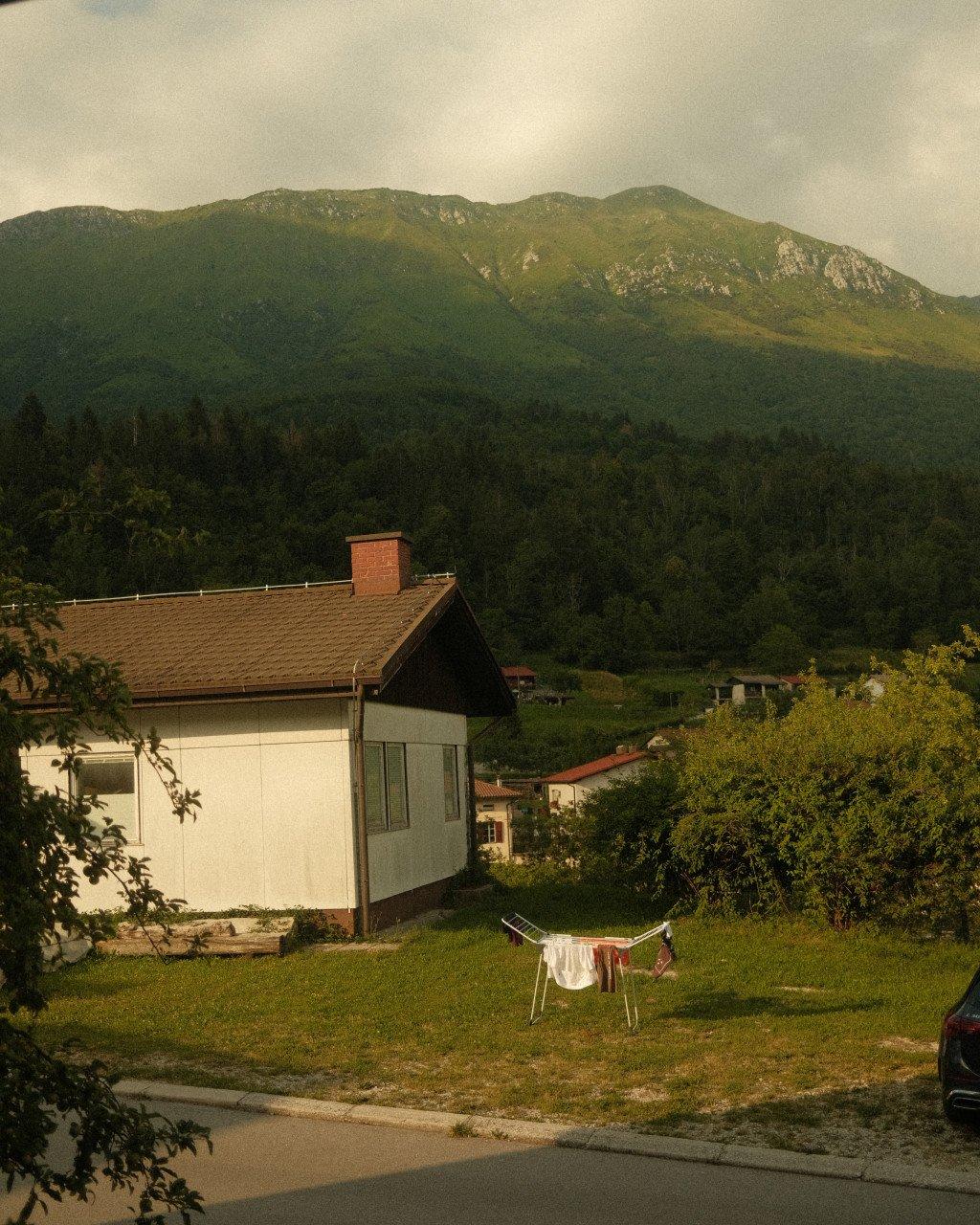Rural Slovenian village with white house and clothesline against forested mountain backdrop