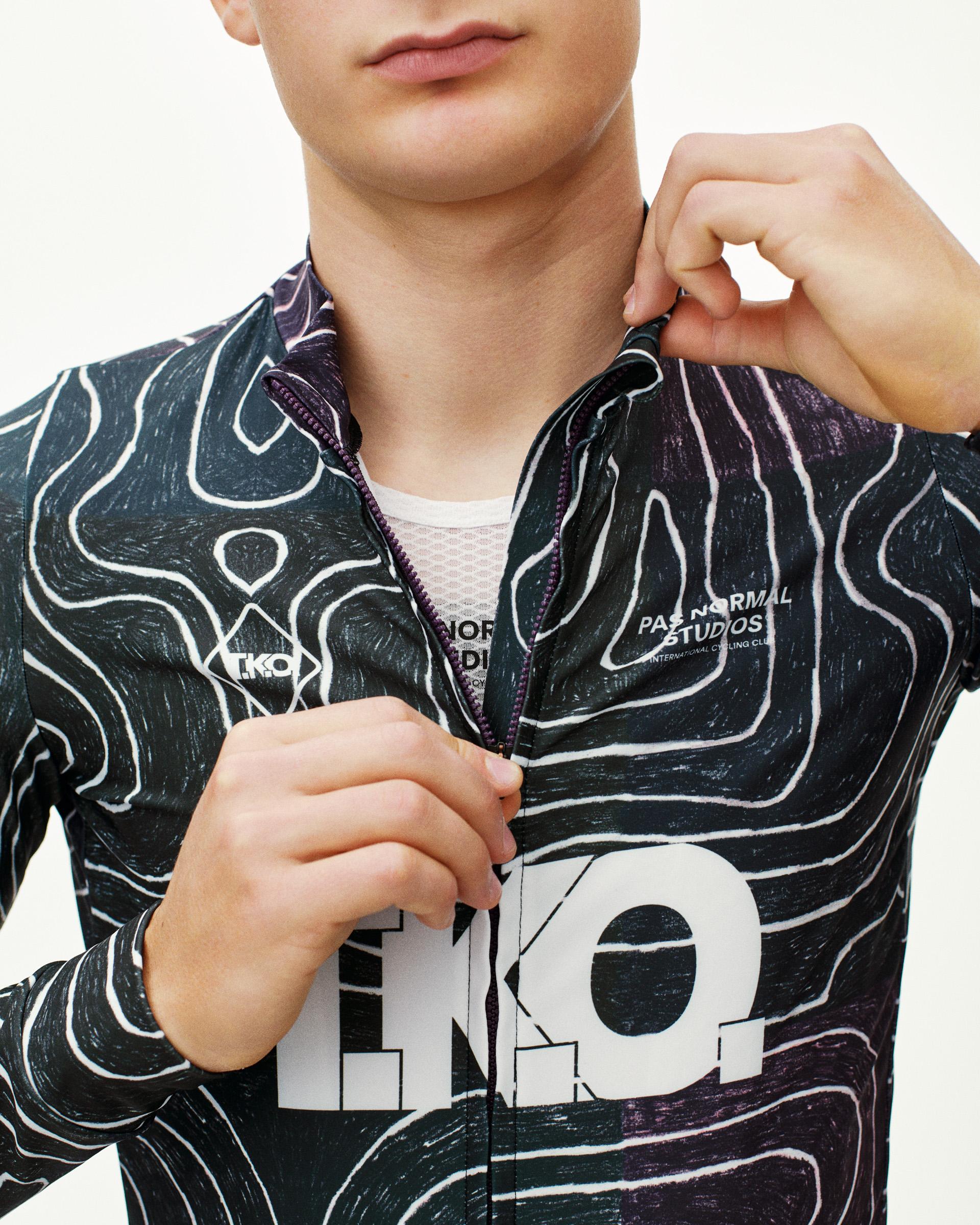 Black Multi T.K.O. Mechanism long sleeve cycling jersey on model, front detail with topographic AOP print and white logo