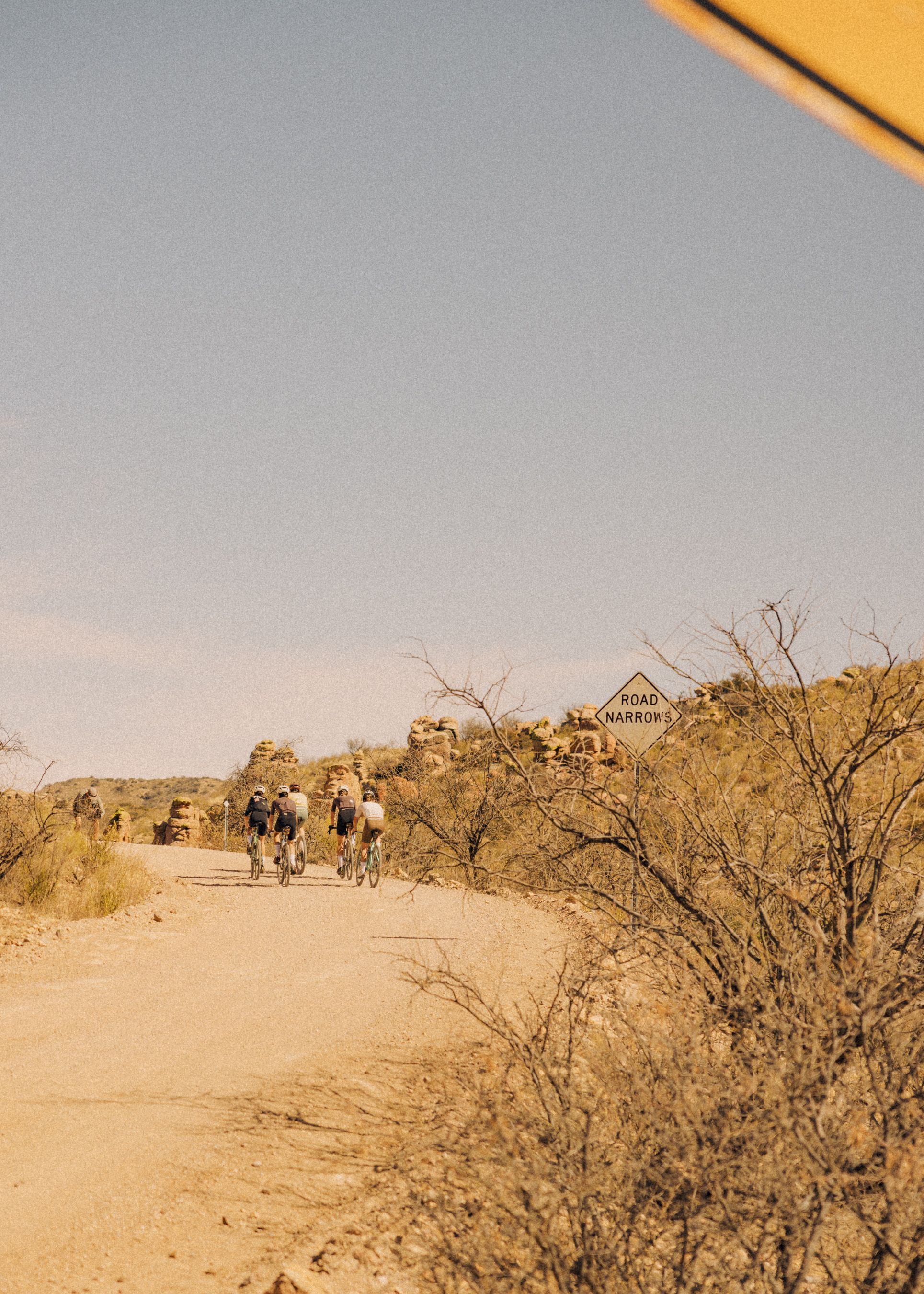 Group of cyclists on gravel road in desert landscape with rocky terrain and sparse vegetation
