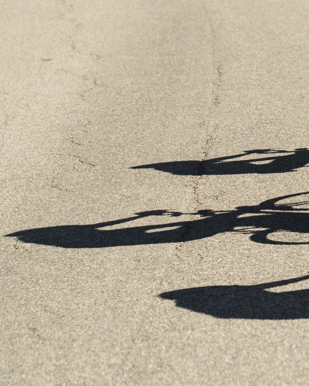 Shadows of cyclists cast on sandy ground
