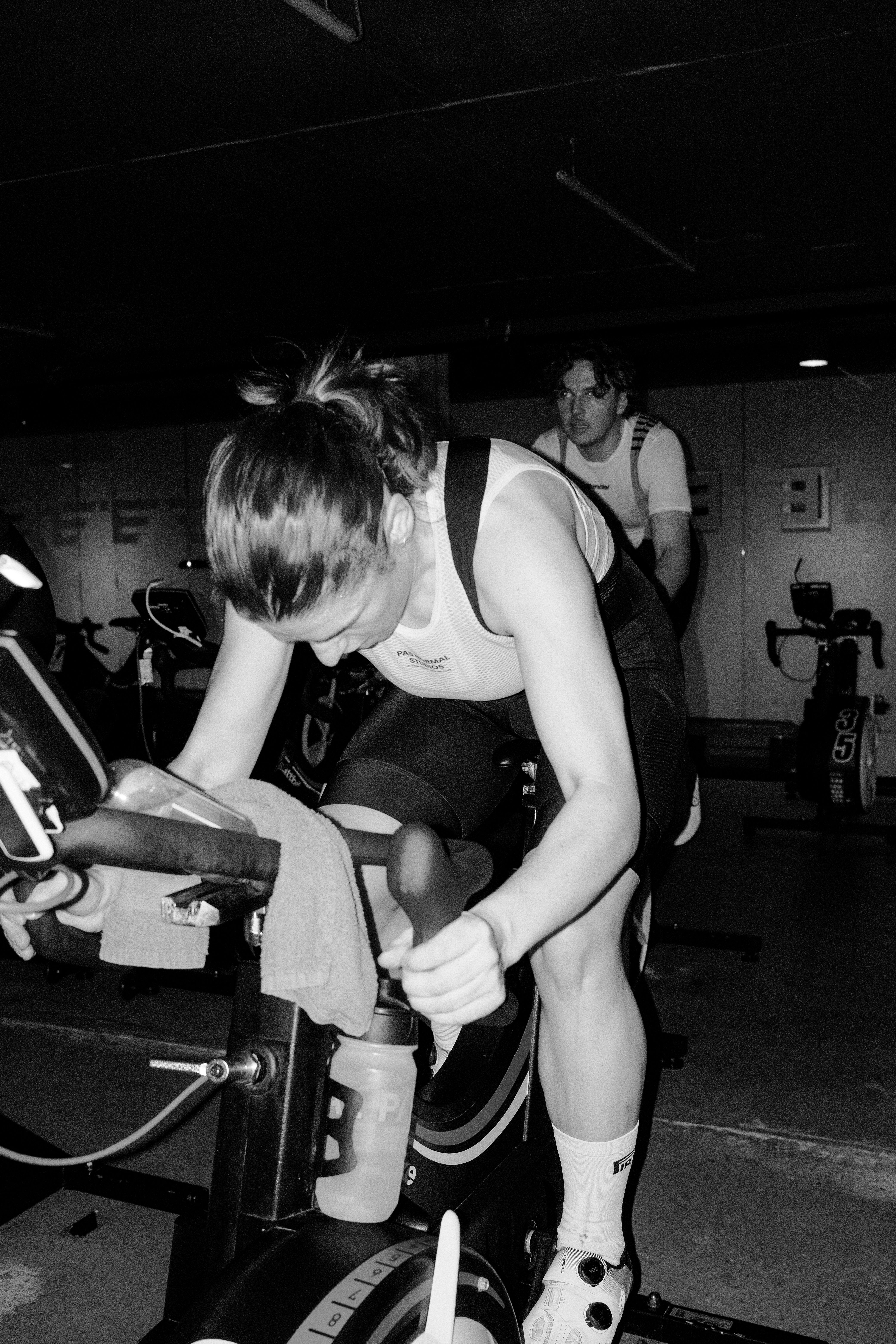 Model wearing white tank top and black shorts training on indoor bike in gym