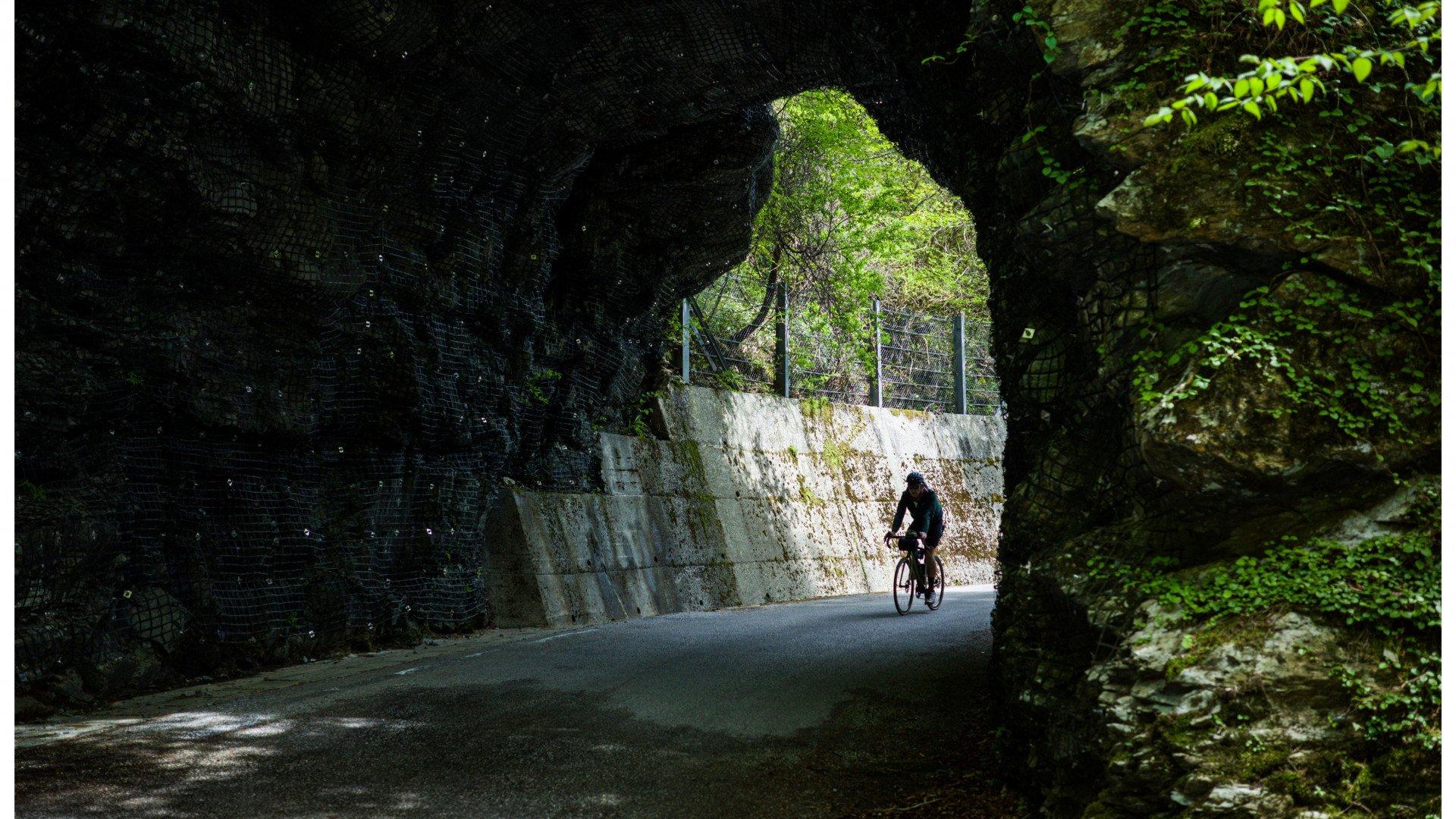Cyclist in dark kit riding through stone tunnel with lush green foliage