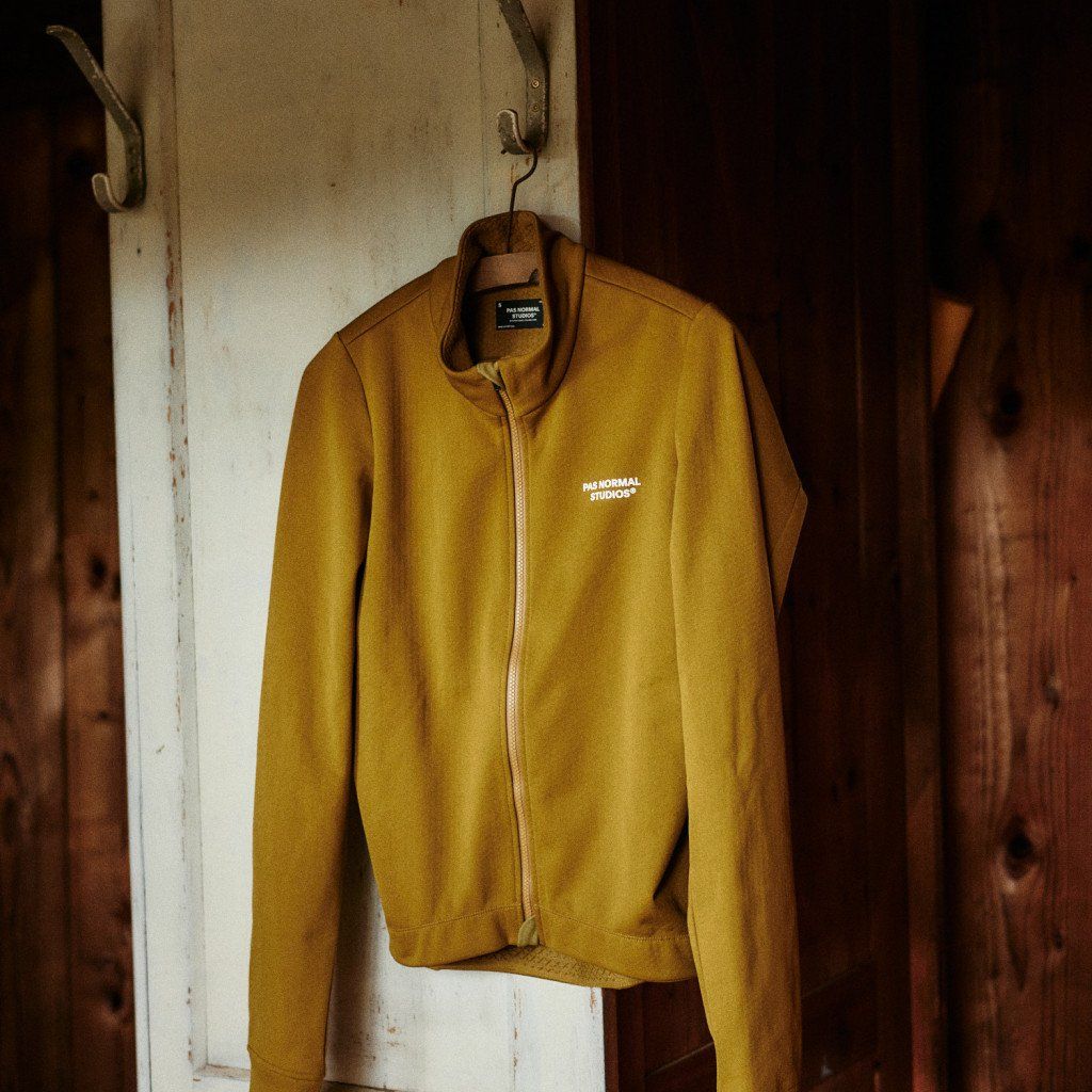 Yellow zip-up jacket with chest lettering hanging on rustic wooden wall