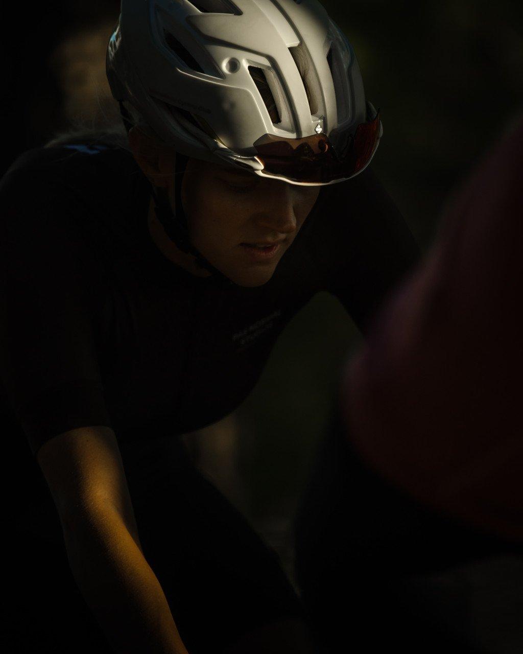Model wearing white aerodynamic cycling helmet with dark visor in dramatic lighting