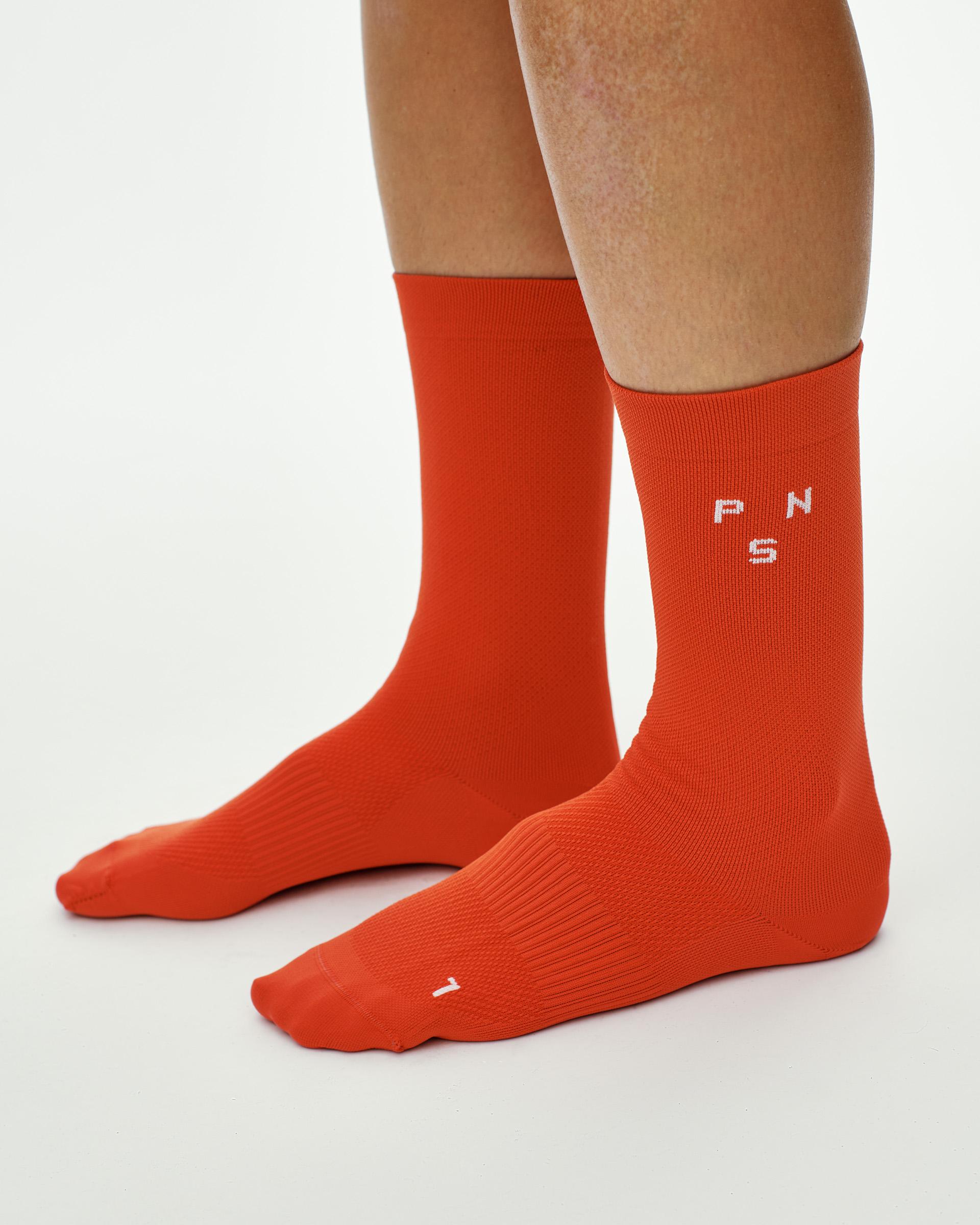 Hibiscus Orange Essential Race cycling socks on model, side view with white logo on ankle