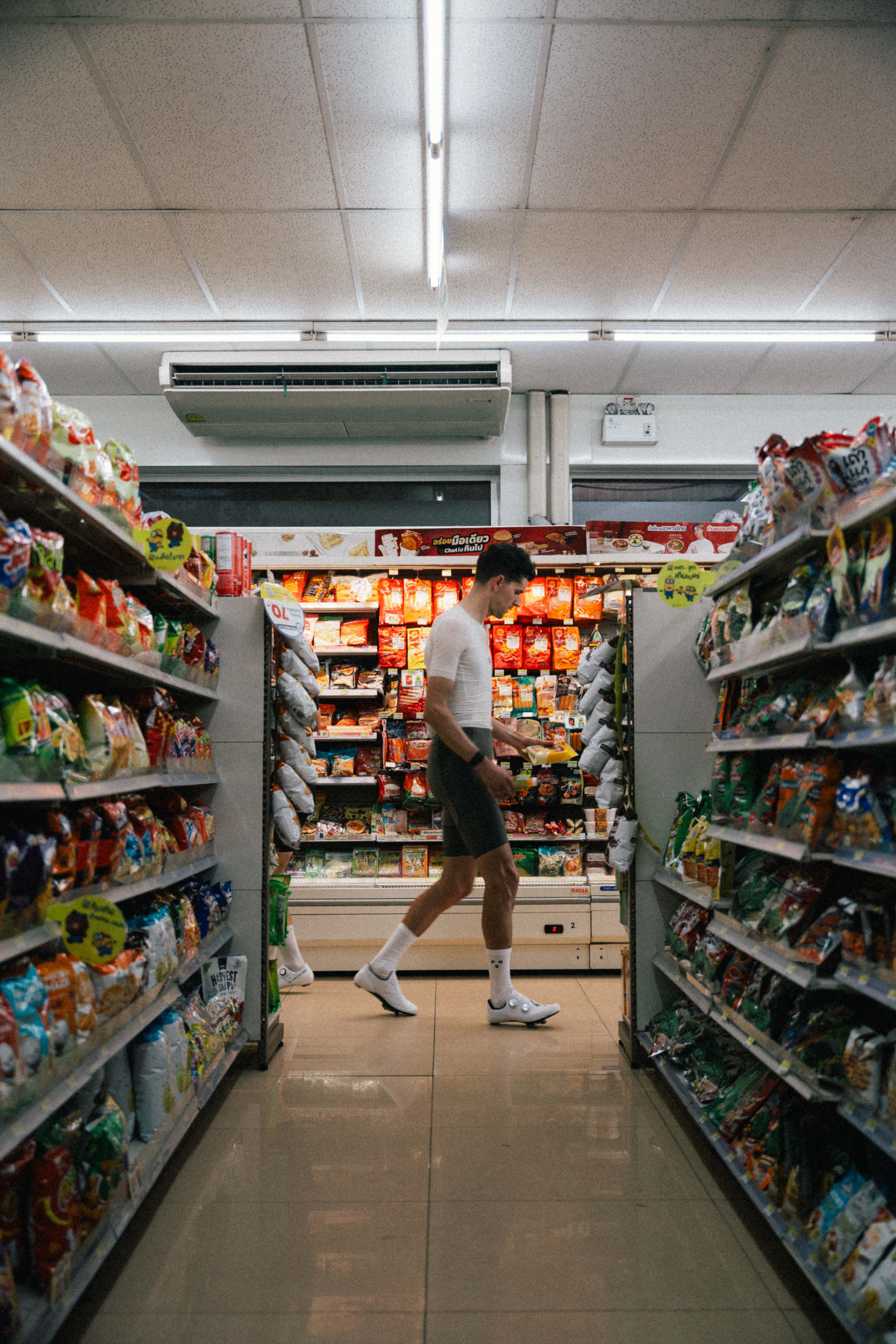 Model wearing beige long-sleeve top and dark shorts shopping in grocery store aisle